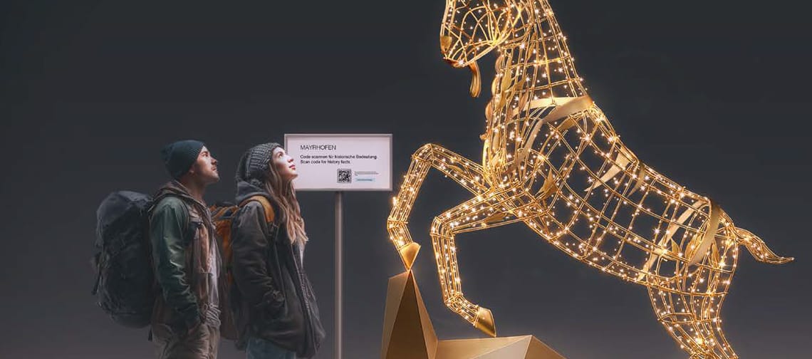 Zwei Wanderer stehen vor einer leuchtenden Steinbock-Lichtskulptur am Fotopoint „6 Orte, 6 Plätze“ in Mayrhofen im Zillertal.