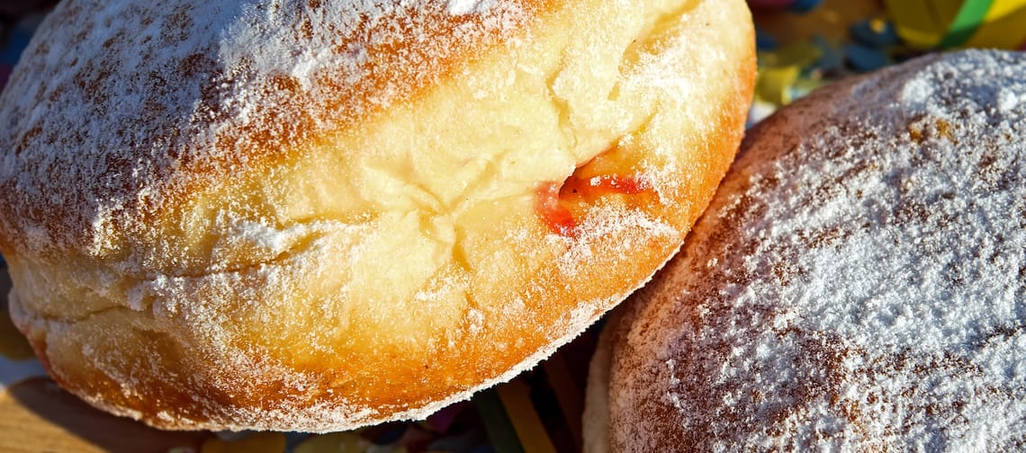 Das Bild zeigt zwei Faschingskrapfen mit Marmelade gefüllt, im Hintergrund Konfetti und bunte Luftschlangen.