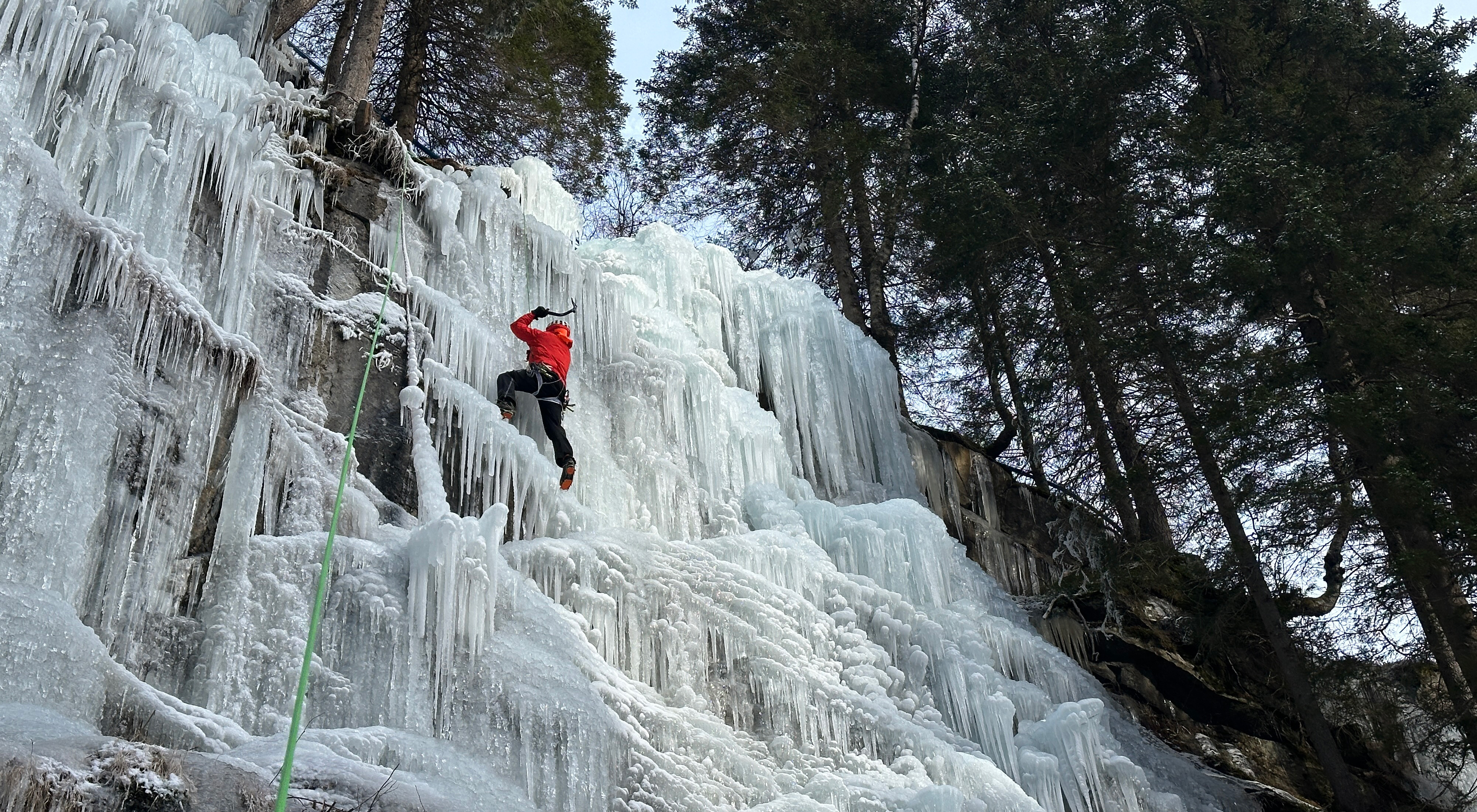 Eiskletterer klettert eine gefrorene Eiswand im Eiskletterpark Zillertal in Ginzling in Tirol, umgeben von winterlicher Fels- und Eislandschaft