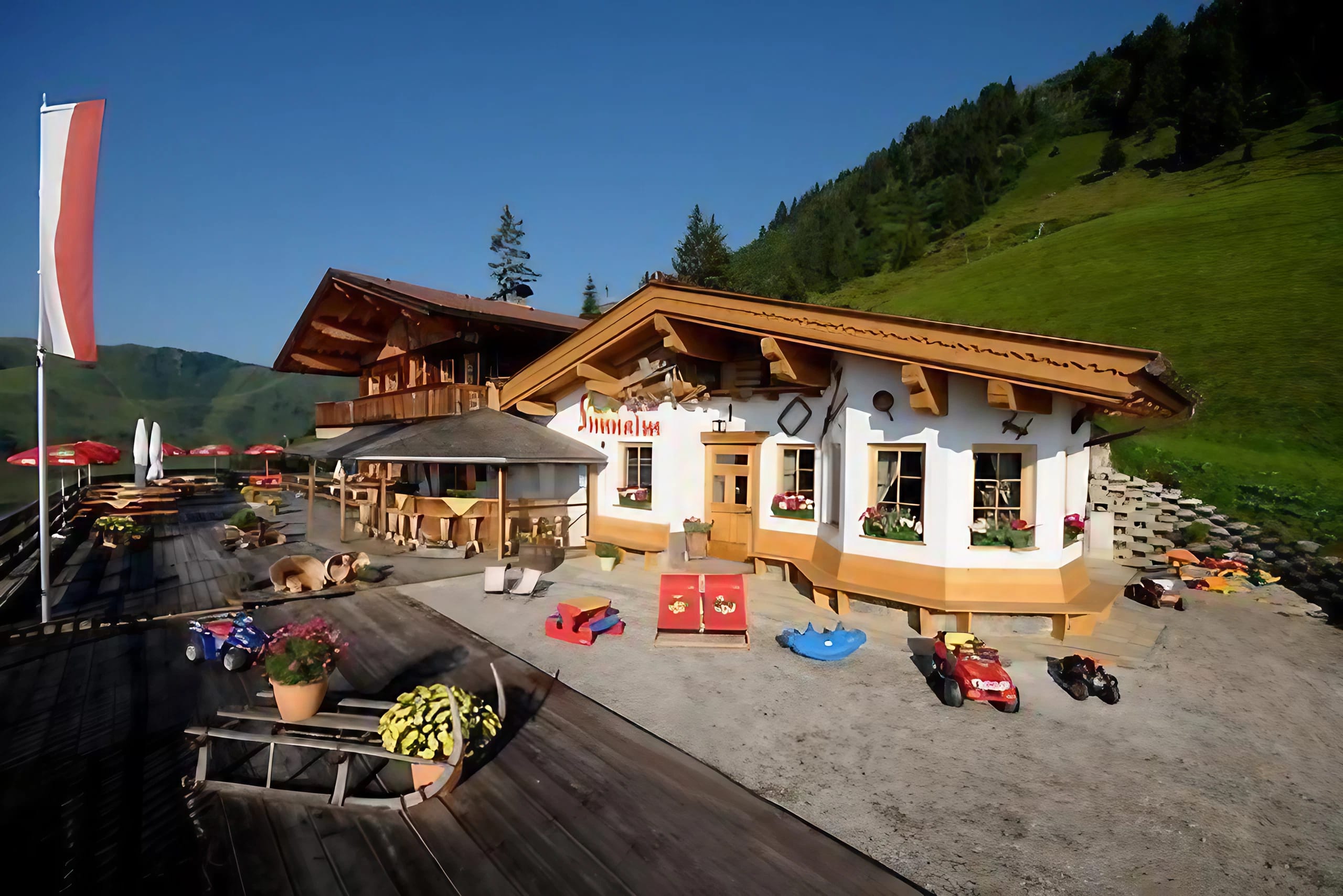 The image shows the Schiestl's Sunnalm in summer, with a terrace and a small playground.