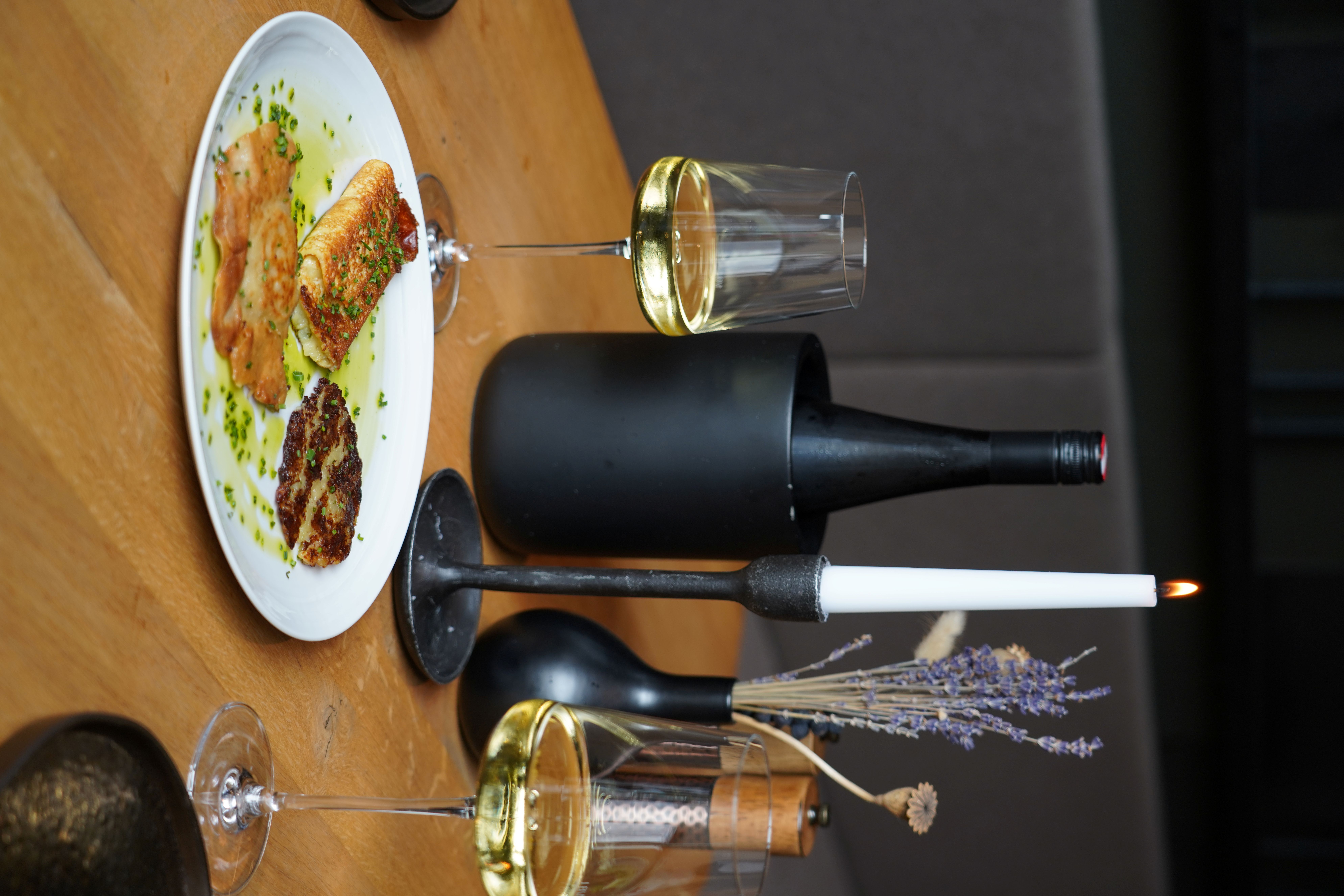 The image shows a variation of appetizers with a glass of white wine and a table candle on a table.