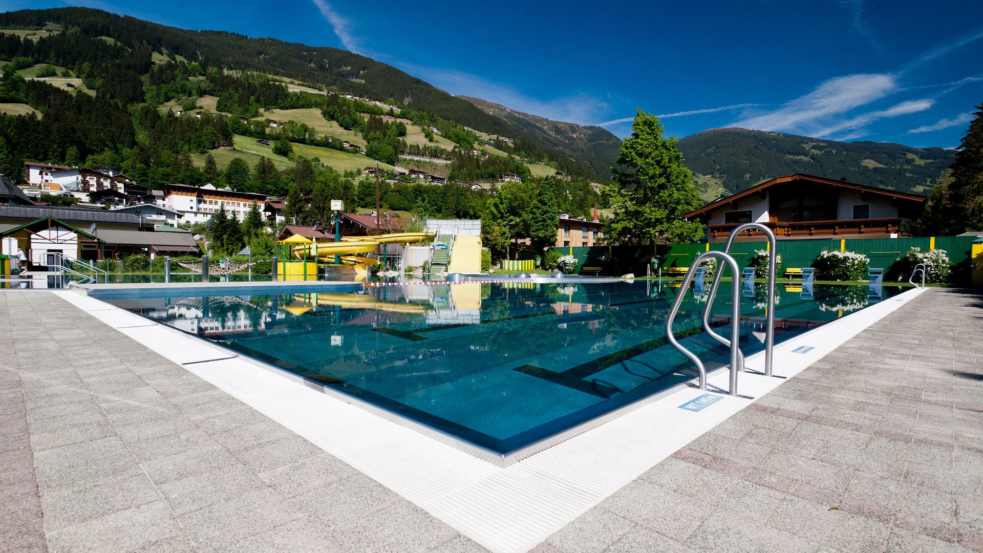 Panoramablick auf das Freibad der Sommerwelt Hippach im Zillertal mit Wasserrutschen, Liegewiese und umliegender Bergkulisse – ideal für Familien und Sonnenanbeter.