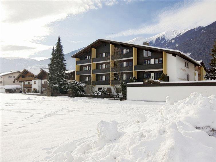 Multi-story modern building in snowy mountain landscape with trees and mountains in the background.