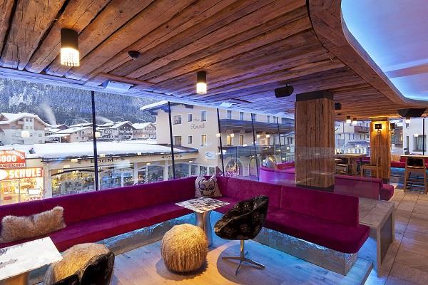 The picture shows the interior of the Harakiri Bar, featuring large windows that allow plenty of natural light. The seating areas are designed in a modern style with warm pink tones, creating a lively and inviting atmosphere.