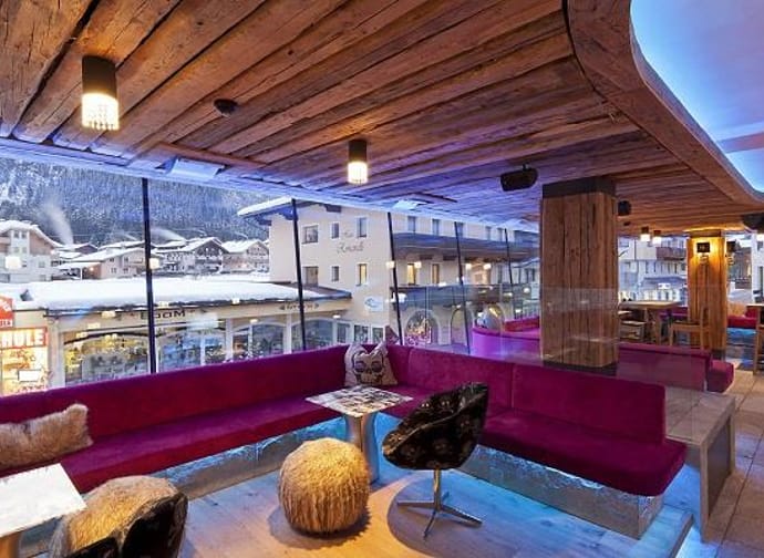 The picture shows the interior of the Harakiri Bar, featuring large windows that allow plenty of natural light. The seating areas are designed in a modern style with warm pink tones, creating a lively and inviting atmosphere.