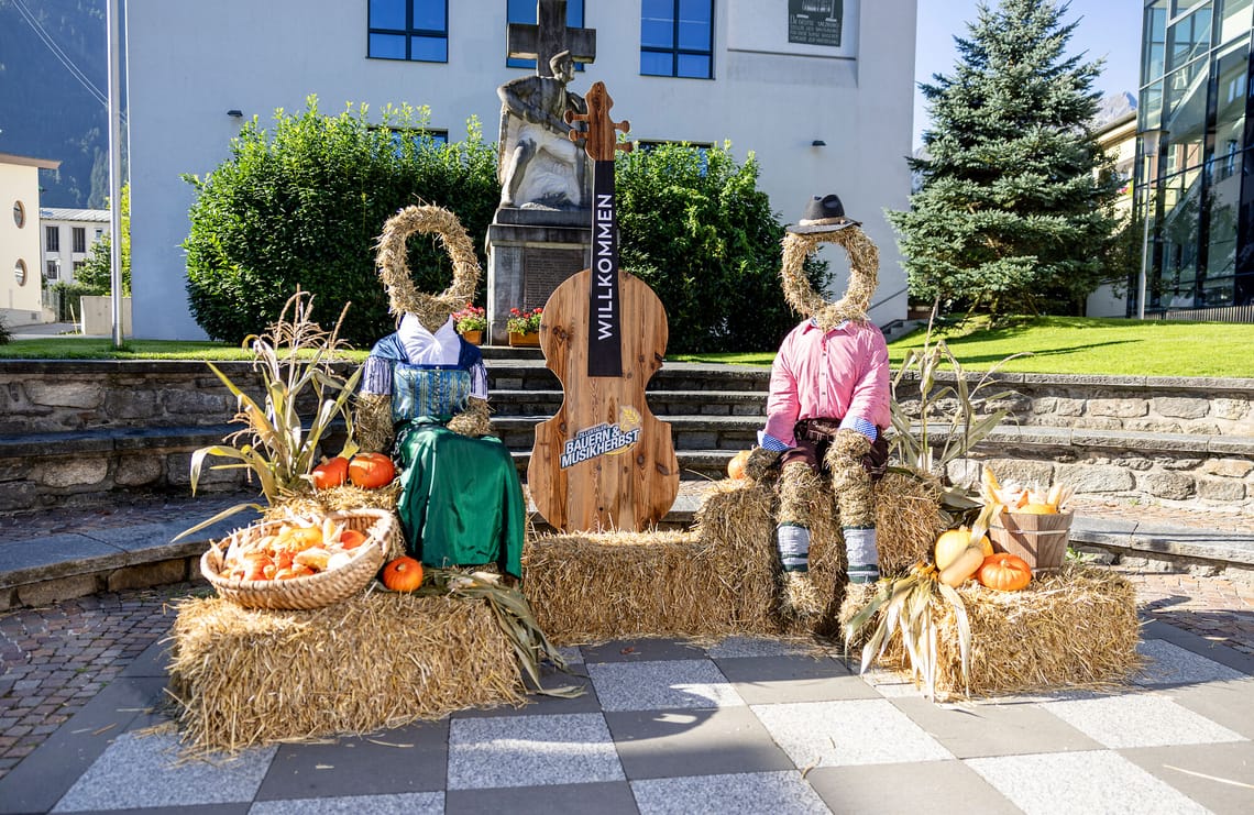 Fotopoint | Zillertaler Bauern- und Musikherbst Fotopoint beim Zillertaler Bauern- und Musikherbst: zwei Heupuppen in Tracht zwischen Heuballen, Kürbissen und herbstlicher Dekoration vor einer traditionellen Bauernhof-Kulisse.