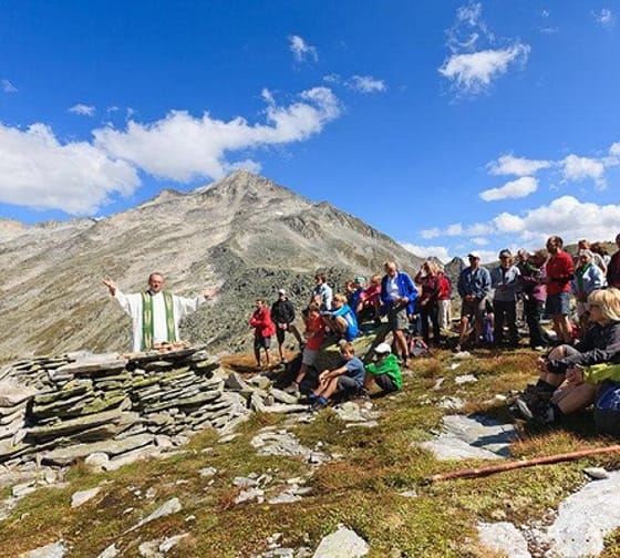 Das Bild zeigt eine Bergmesse mit Pfarrer und Gläubigen auf dem Hundskehljoch, die eine hl. Messe feiern.