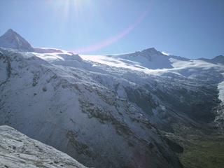 Snow-covered mountain peaks with glaciers under a clear sky, sunlight reflecting off the snow.