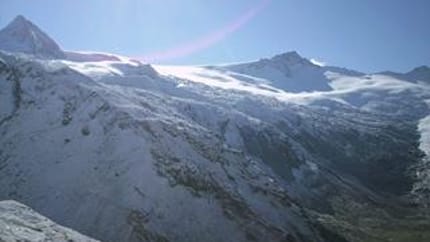 Snow-covered mountain peaks with glaciers under a clear sky, sunlight reflecting off the snow.