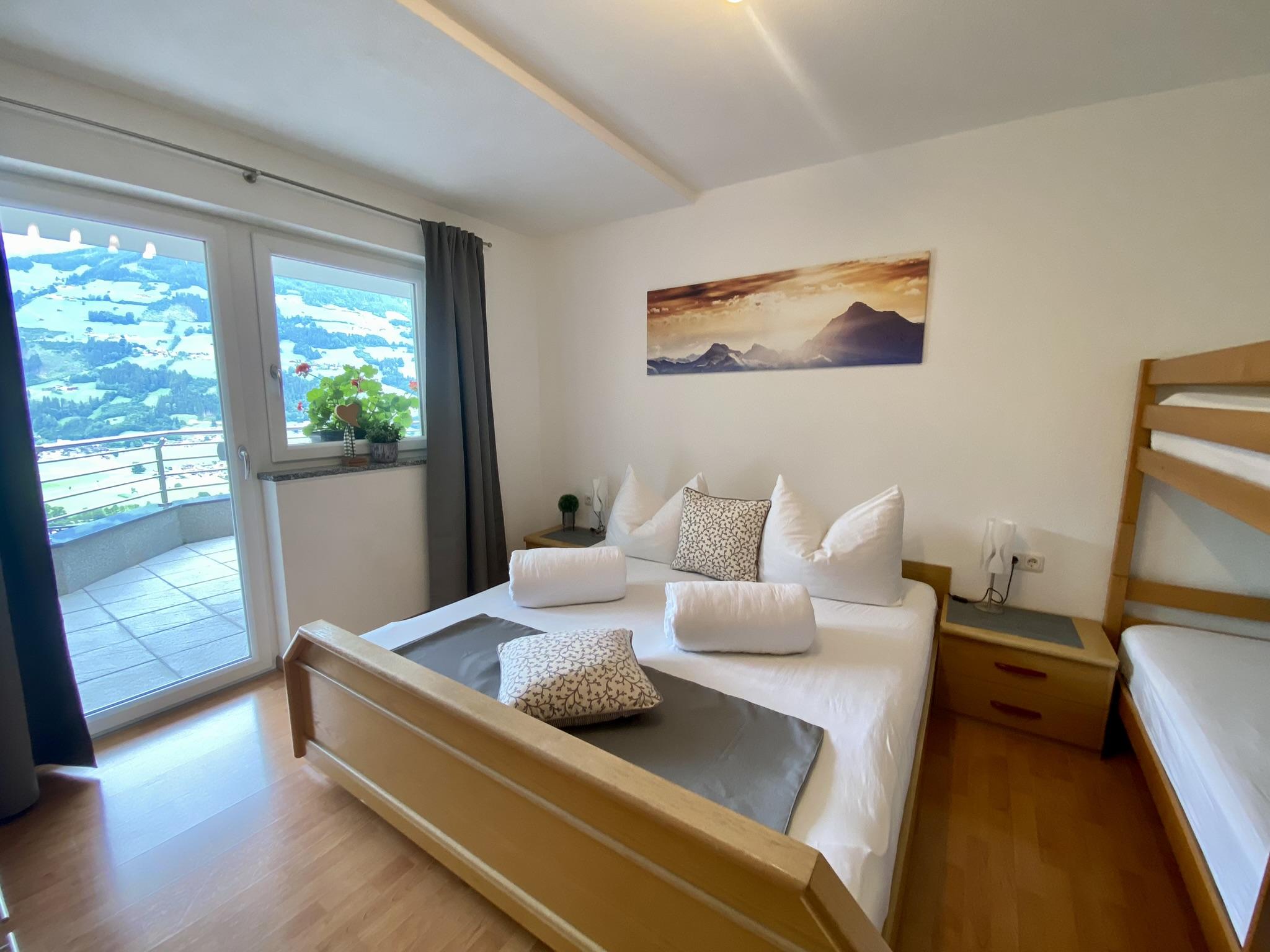 A bedroom with a bed, pillows, wall art, and a balcony view of mountains, curtains, and plants.