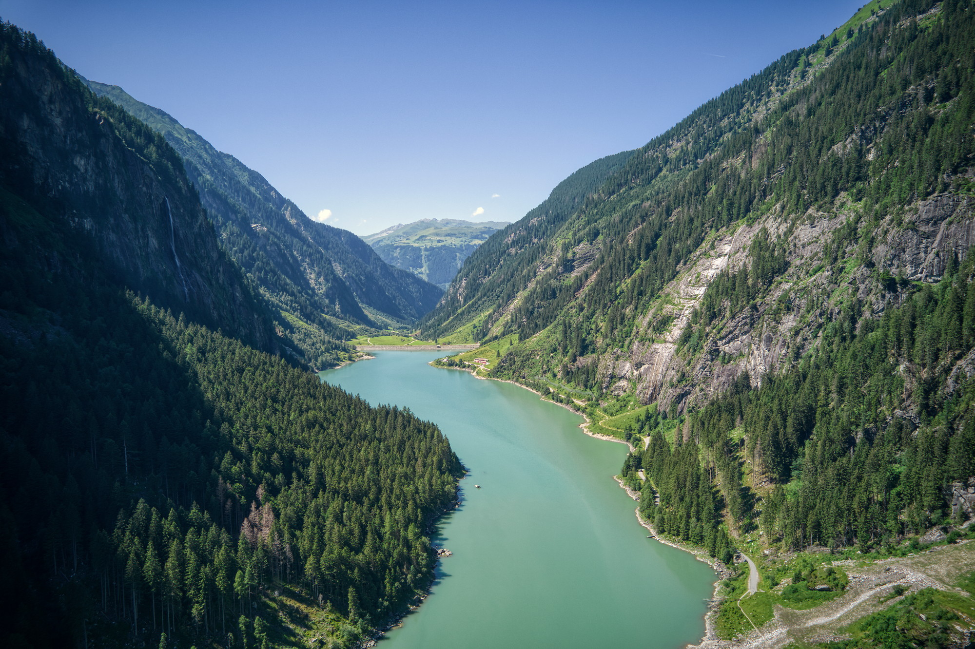 Ein großer Stausee mit blau grünem Wasser, umgeben von Bergen und Wald