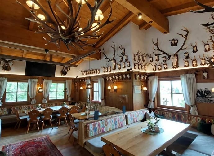 Rustic dining room with wooden ceiling, walls, and floor, decorated with antlers and trophies, large table, cozy atmosphere.