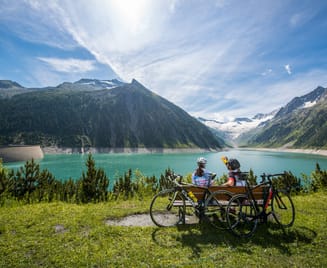 Rennradfahrer rasten am Schlegeis Speicher mit Blick auf türkisfarbenes Wasser und umliegende Alpen – Sommerliche Auszeit in der Zillertaler Bergwelt.