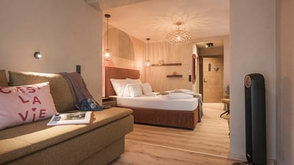Gemütliches Schlafzimmer mit Bett, Sofa, Lampen und Holzwand, warme Beleuchtung, Schuhe am Boden.