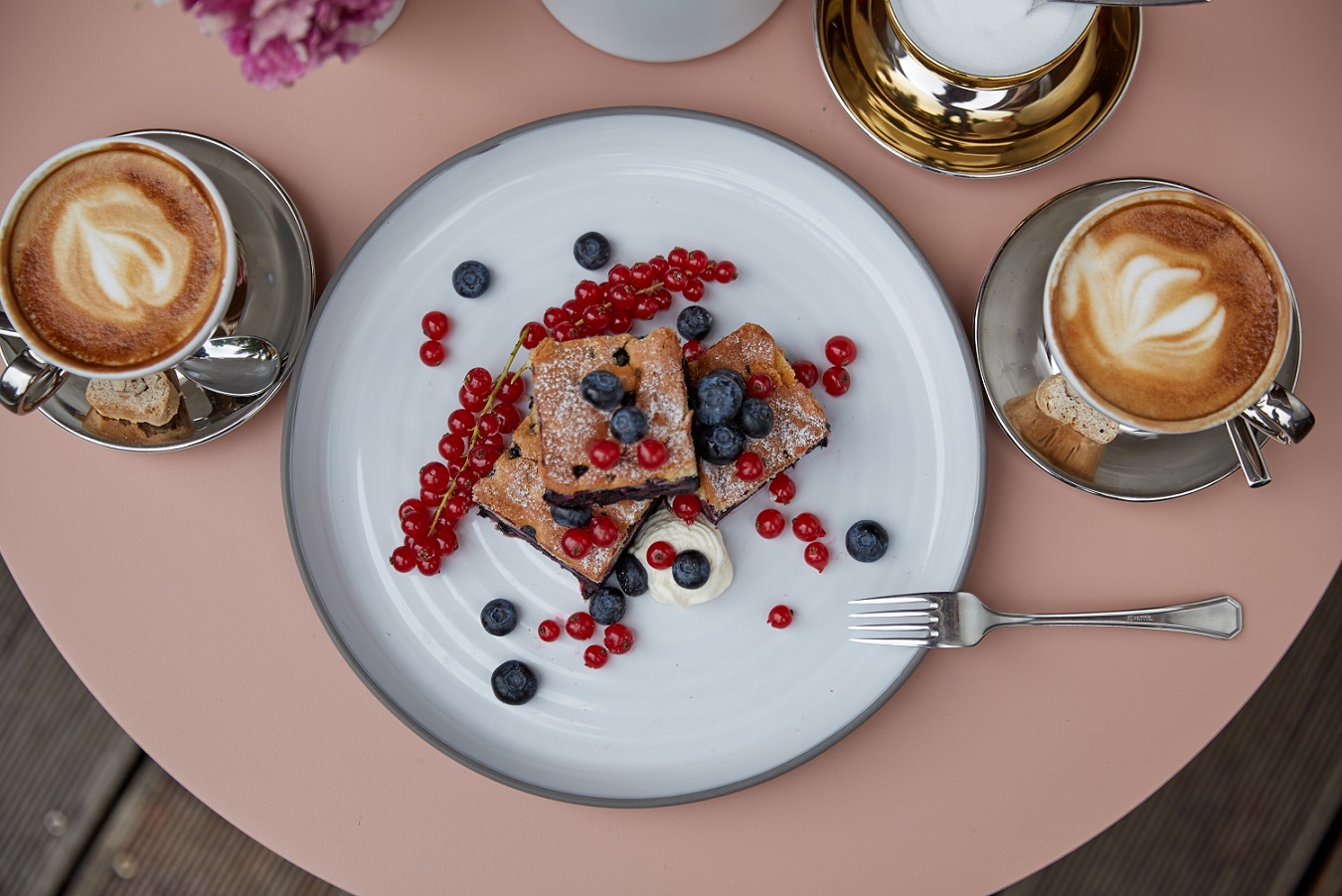 Breakfast table with blueberries, red currants, waffles, two coffees with foam, sugar, and a spoon
