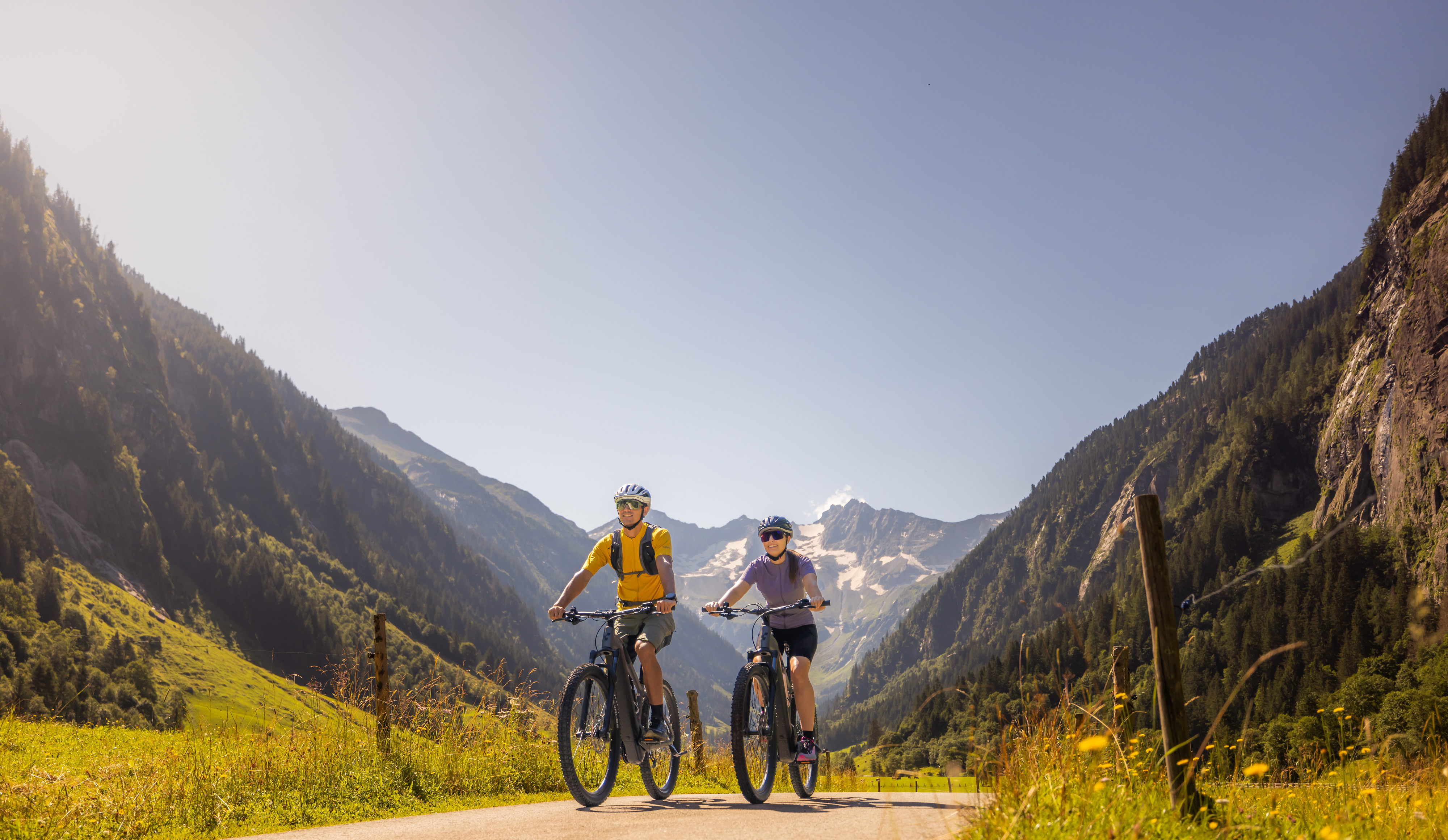 Mittelschwere Fahrradtour im Stilluptal bei Mayrhofen-Hippach im Zillertal: zwei Personen fahren entspannt auf einem breiten Weg durch grüne Wiesen, umgeben von Bergen unter blauem Himmel.