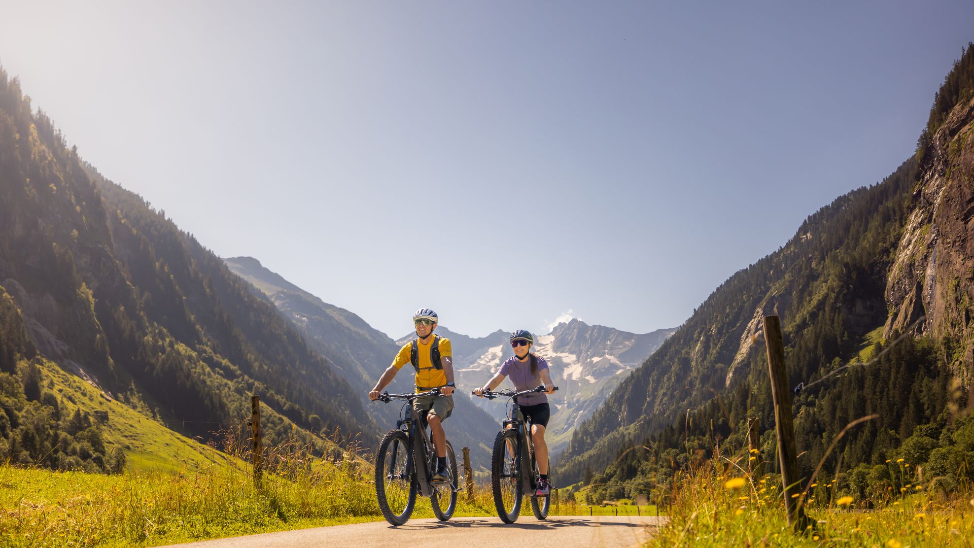 Mittelschwere Fahrradtour im Stilluptal bei Mayrhofen-Hippach im Zillertal: zwei Personen fahren entspannt auf einem breiten Weg durch grüne Wiesen, umgeben von Bergen unter blauem Himmel.