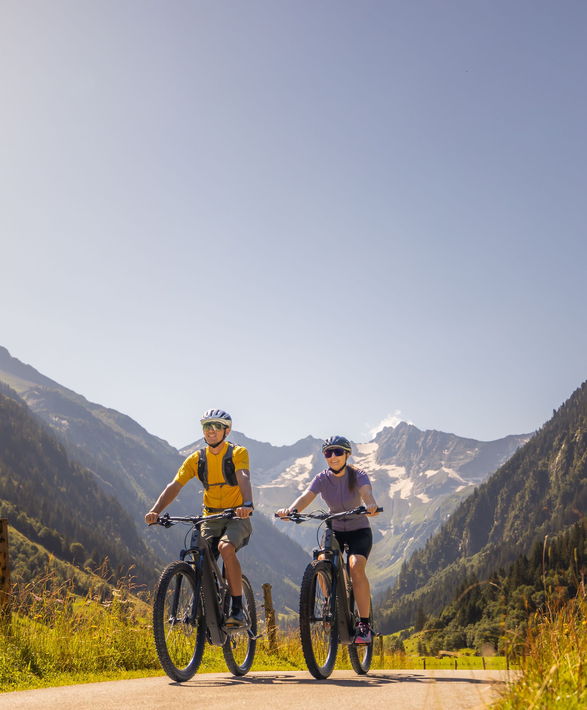 Mittelschwere Fahrradtour im Stilluptal bei Mayrhofen-Hippach im Zillertal: zwei Personen fahren entspannt auf einem breiten Weg durch grüne Wiesen, umgeben von Bergen unter blauem Himmel.