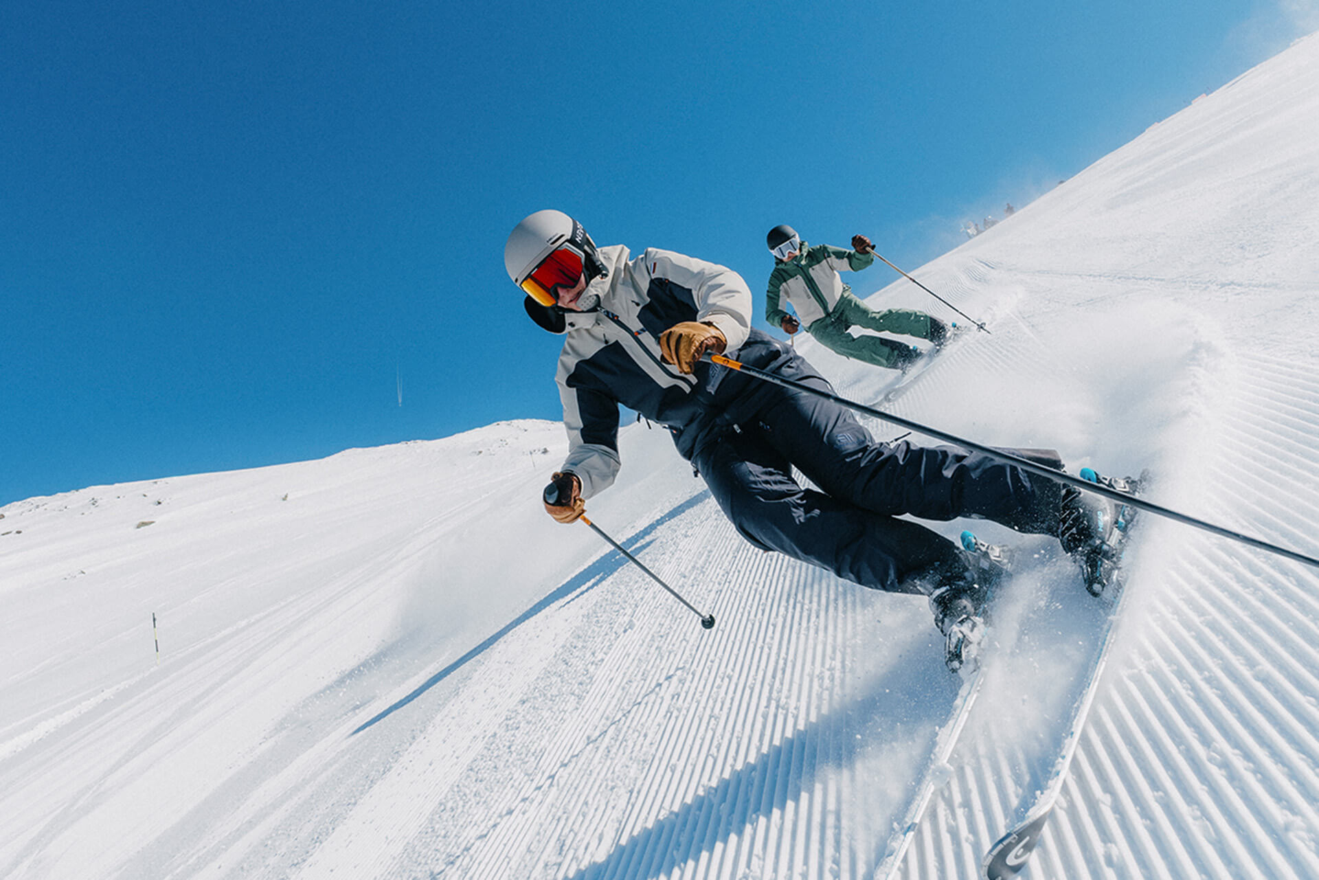 Zwei Skifahrer in bunten Jacken fahren die Piste hinunter auf schneebedecktem Berg.