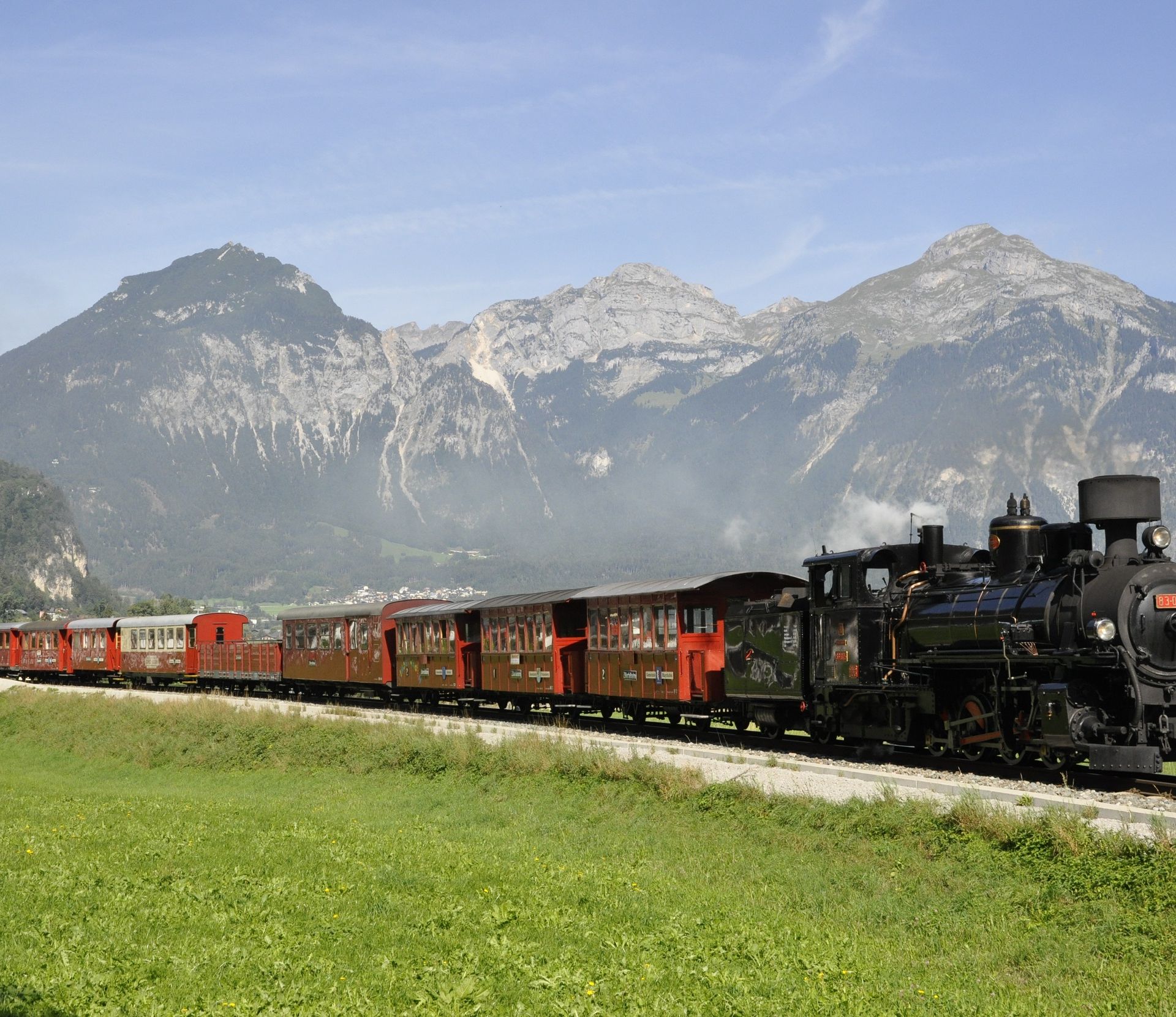 „Ein nostalgischer Dampfzug der Zillertalbahn fährt durch grüne Wiesen vor imposanter Bergkulisse – ein Highlight für Jung und Alt im Zillertal.