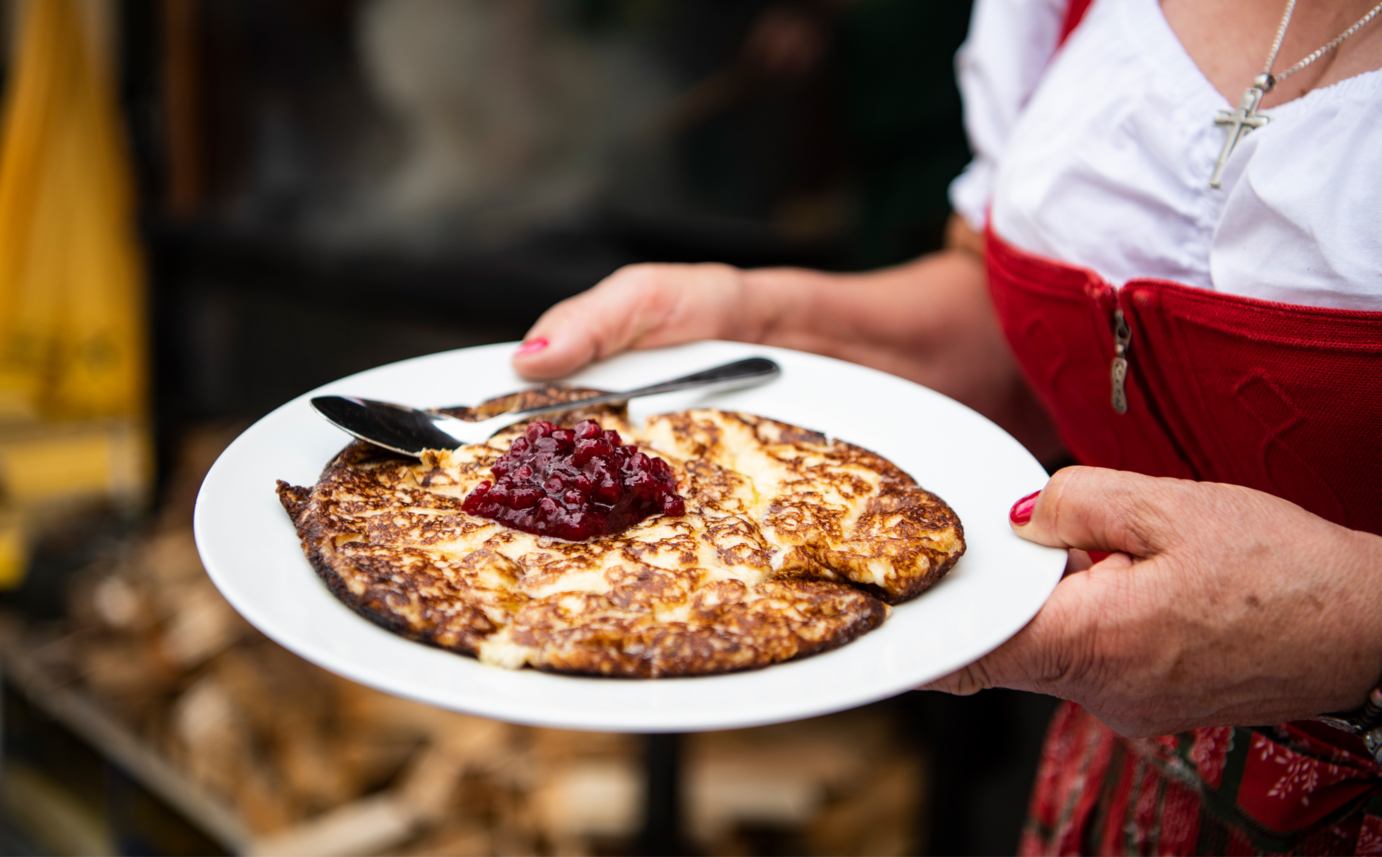 Eine Person in Tracht hält einen Teller mit Melchermuas, einer Zillertaler Spezialität, serviert mit Preiselbeermarmelade in der Mitte.