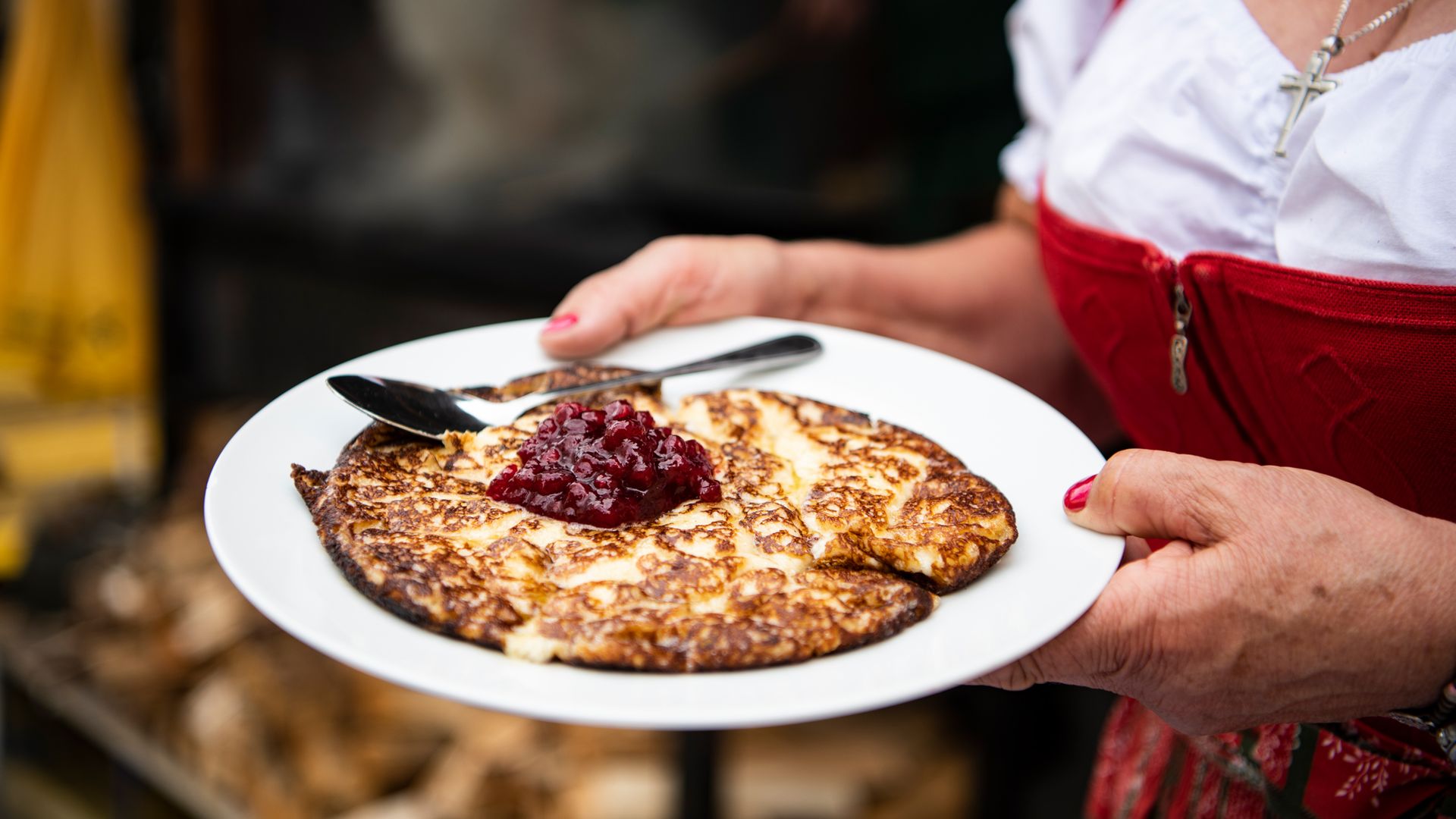 Eine Person in Tracht hält einen Teller mit Melchermuas, einer Zillertaler Spezialität, serviert mit Preiselbeermarmelade in der Mitte.