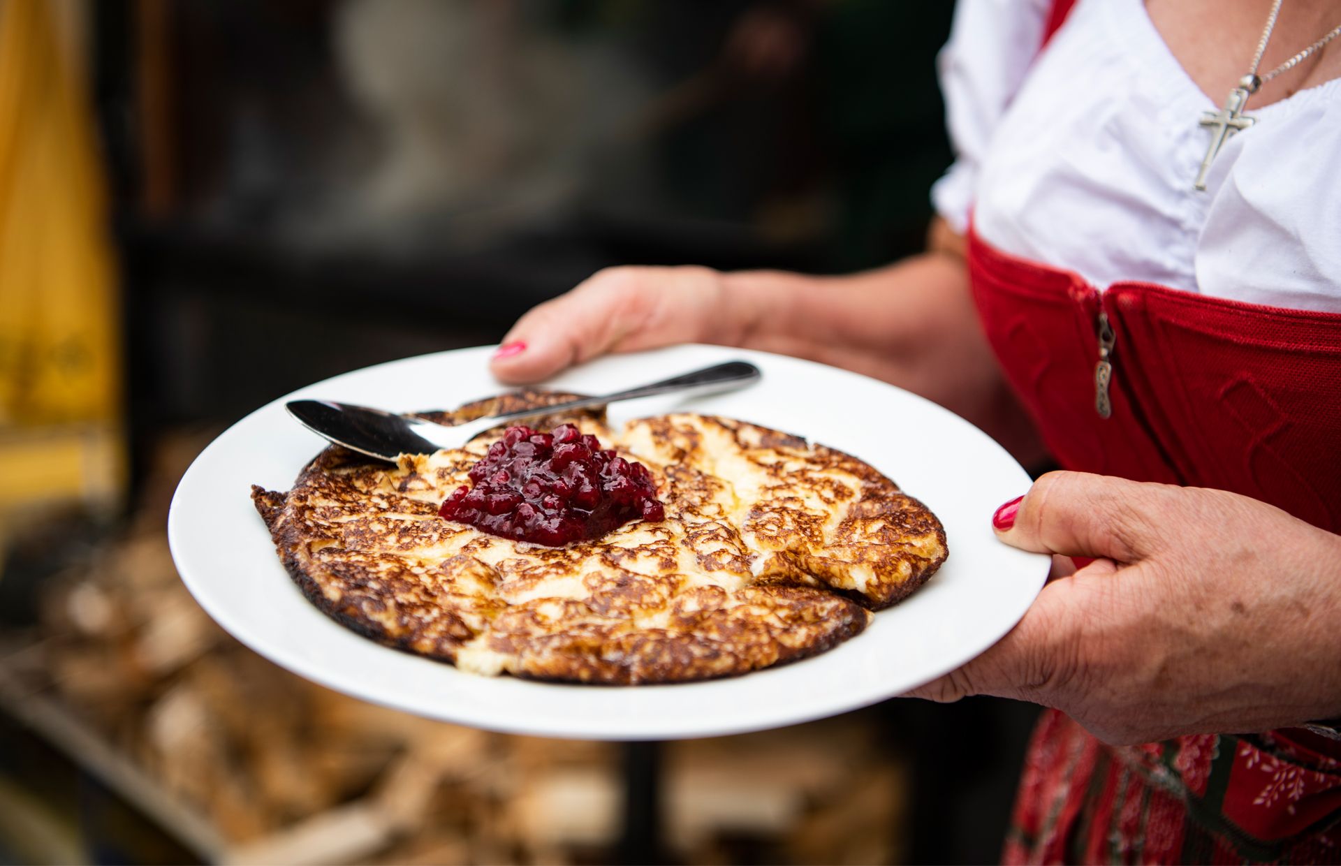 A person in traditional dress holds a plate of Melchermuas, a Tyrolean specialty, served with lingonberry jam in the center.