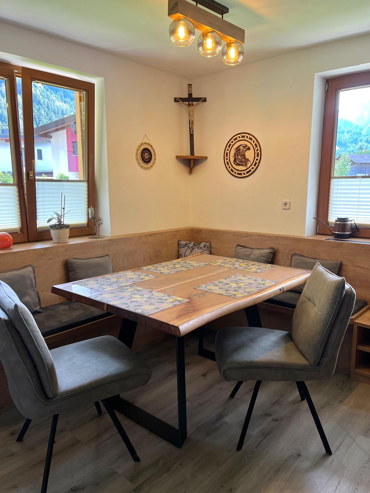 A dining room with a wooden table, six chairs, two windows, wall decorations, and a ceiling light.
