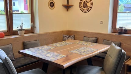 A dining room with a wooden table, six chairs, two windows, wall decorations, and a ceiling light.