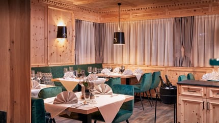 A cozy dining room with wooden walls, green velvet chairs, and tables set with white tablecloths.