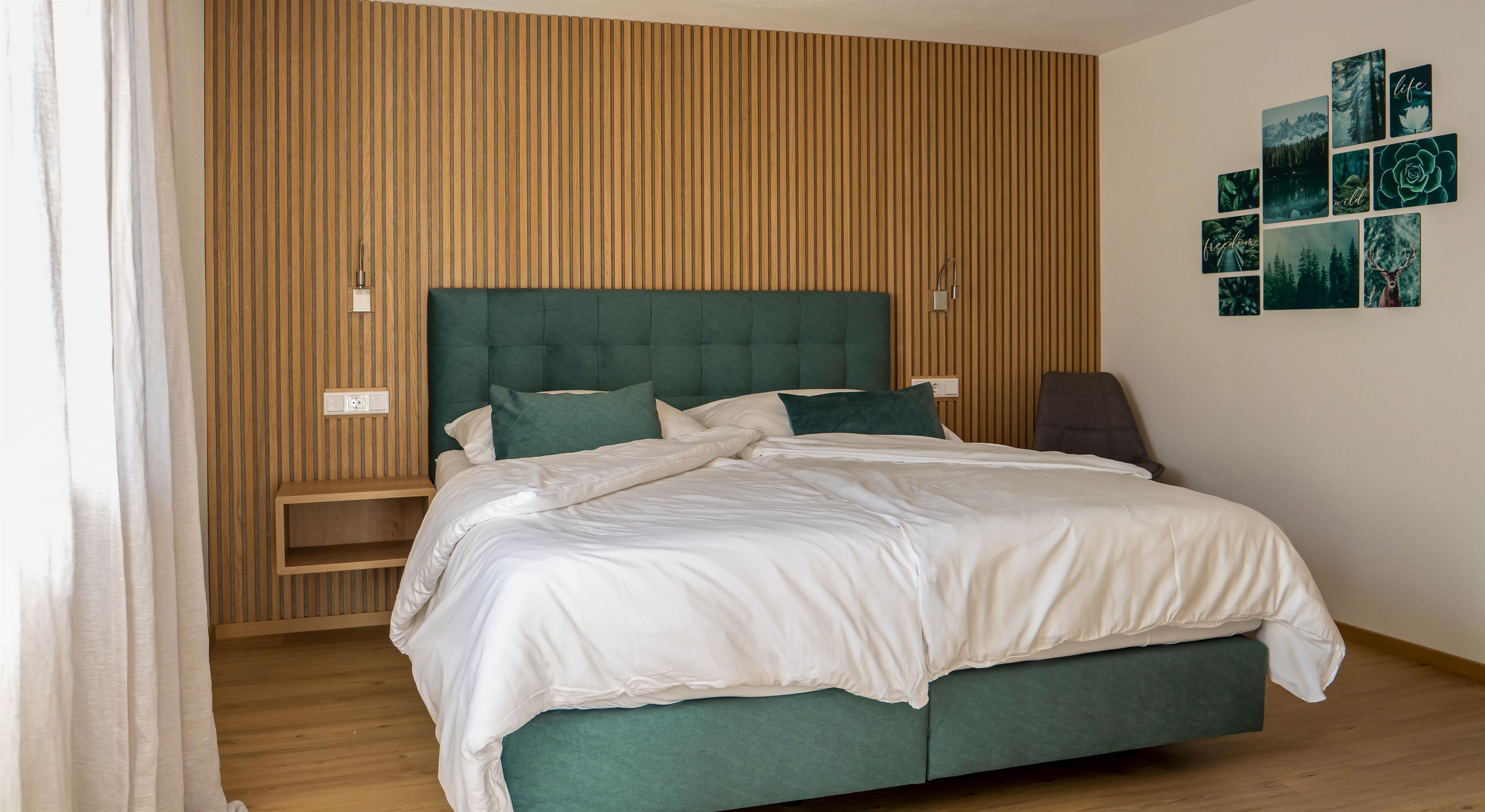 Ein modernes Schlafzimmer mit grünem gepolstertem Bett, Holzvertäfelung und Wandbildern mit Naturmotiven.