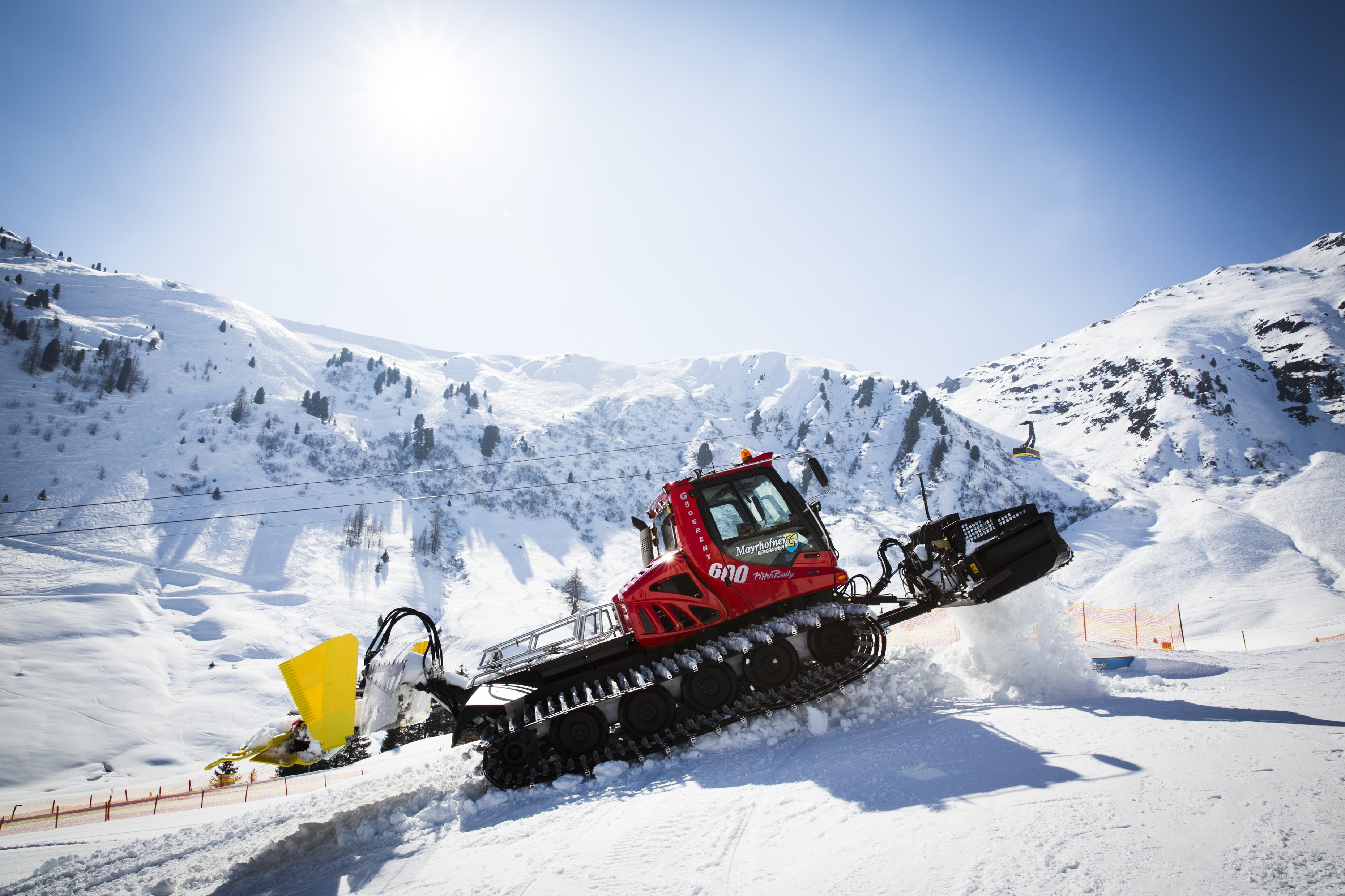 Snowmobile on snowy mountain under bright sun, with ski lift and winter landscape in the background.