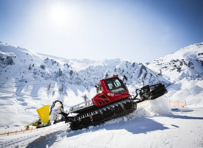 Snowmobile on snowy mountain under bright sun, with ski lift and winter landscape in the background.