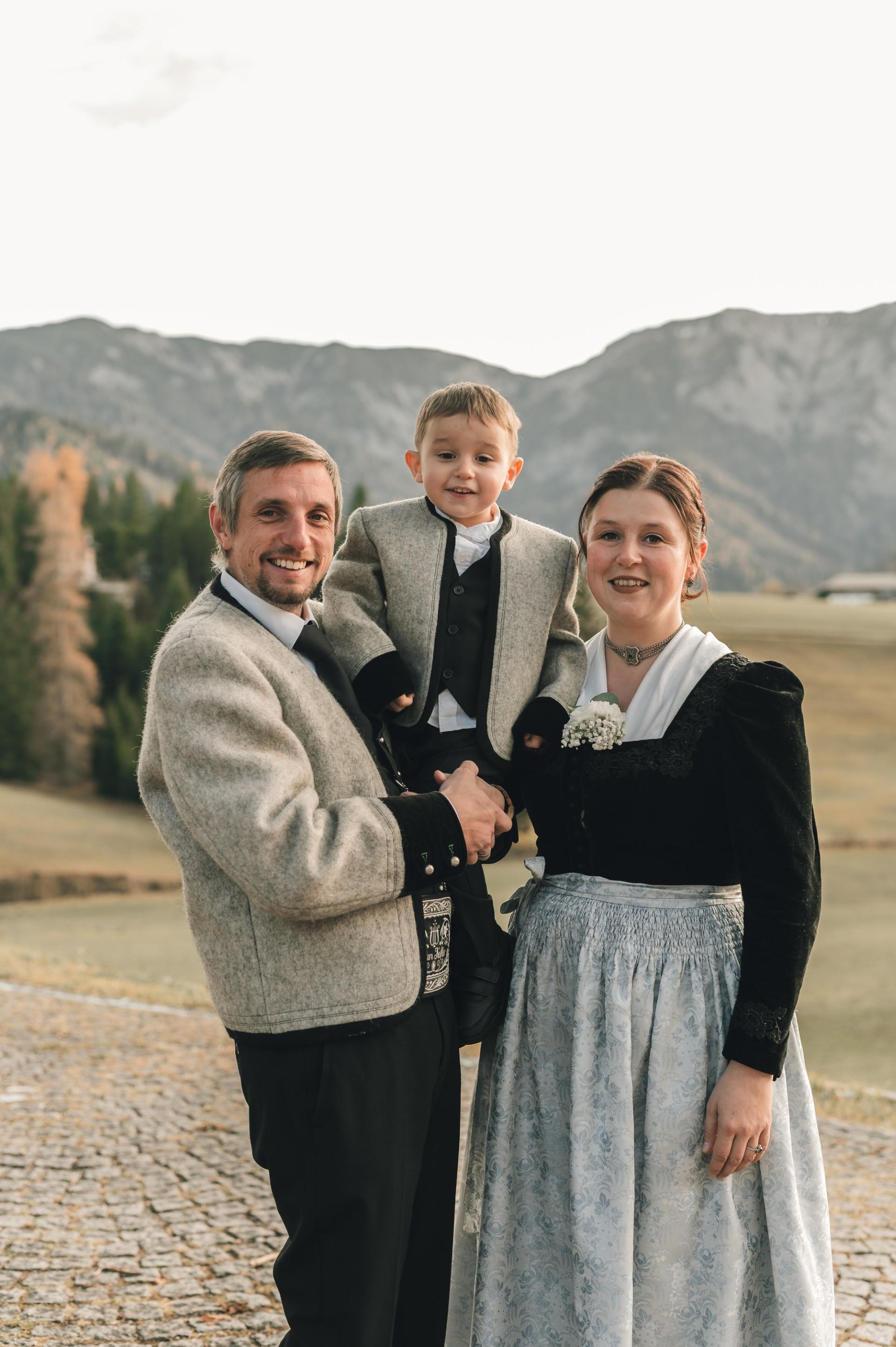 Familie im traditionellen Kleidung vor Bergen, lächelnd, bei schönem Wetter im Freien.