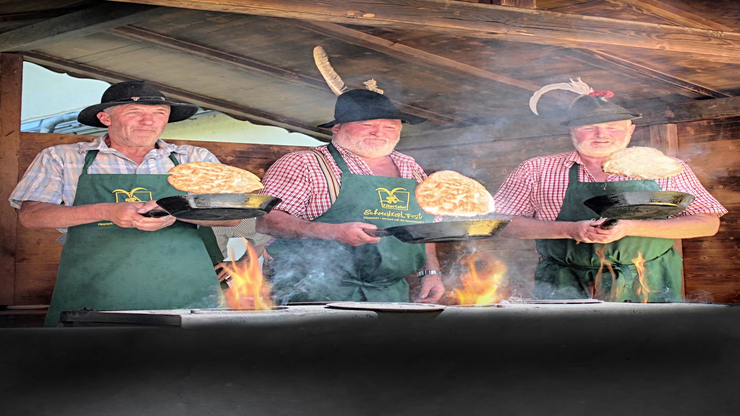 The image shows three men in traditional clothing cooking “Muas” in front of a stove.