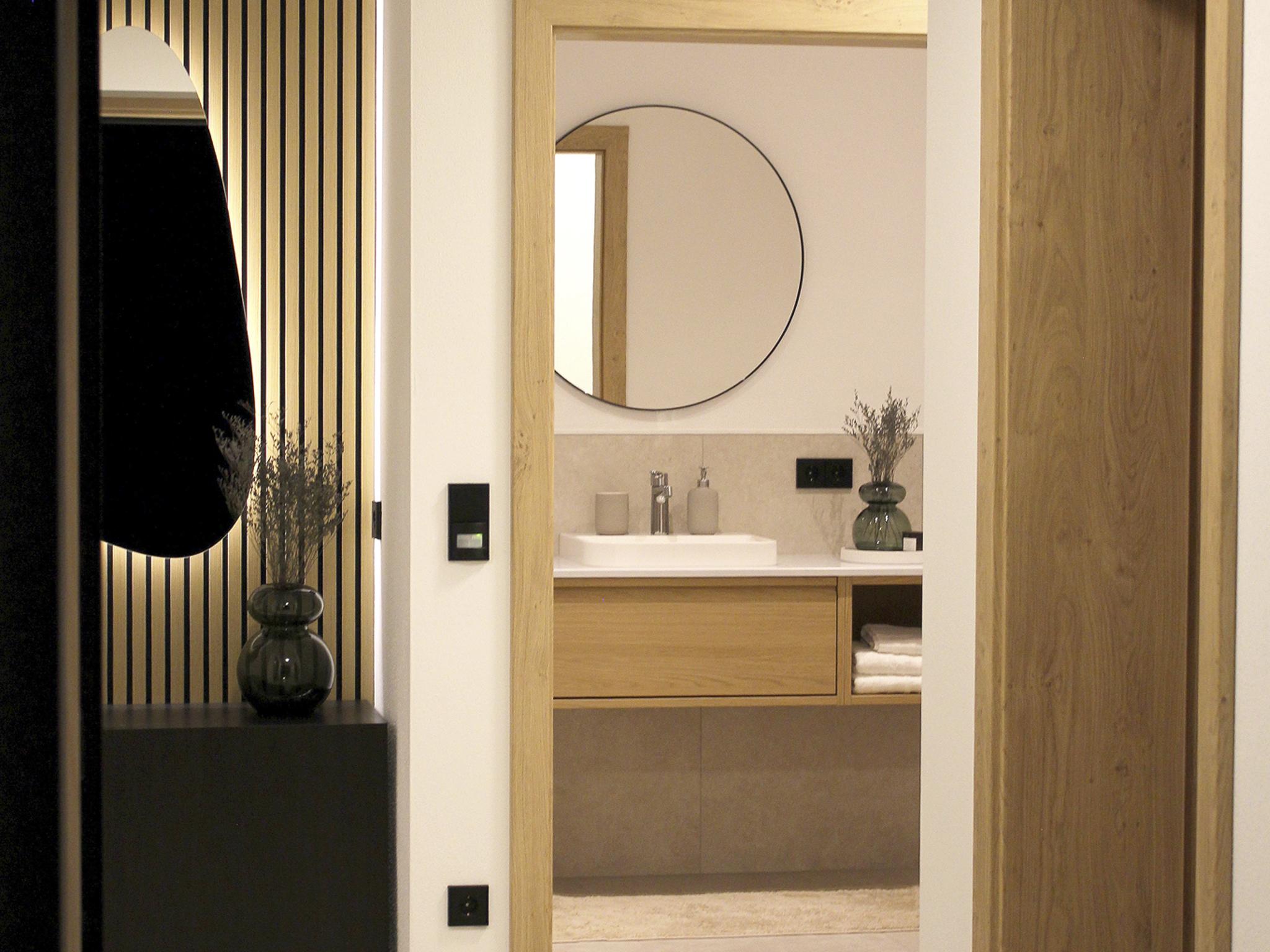 Ein Spiegel im Badezimmer mit Holzrahmen, daneben eine Vase mit Zweigen, dunkle Wandpaneele im Hintergrund.