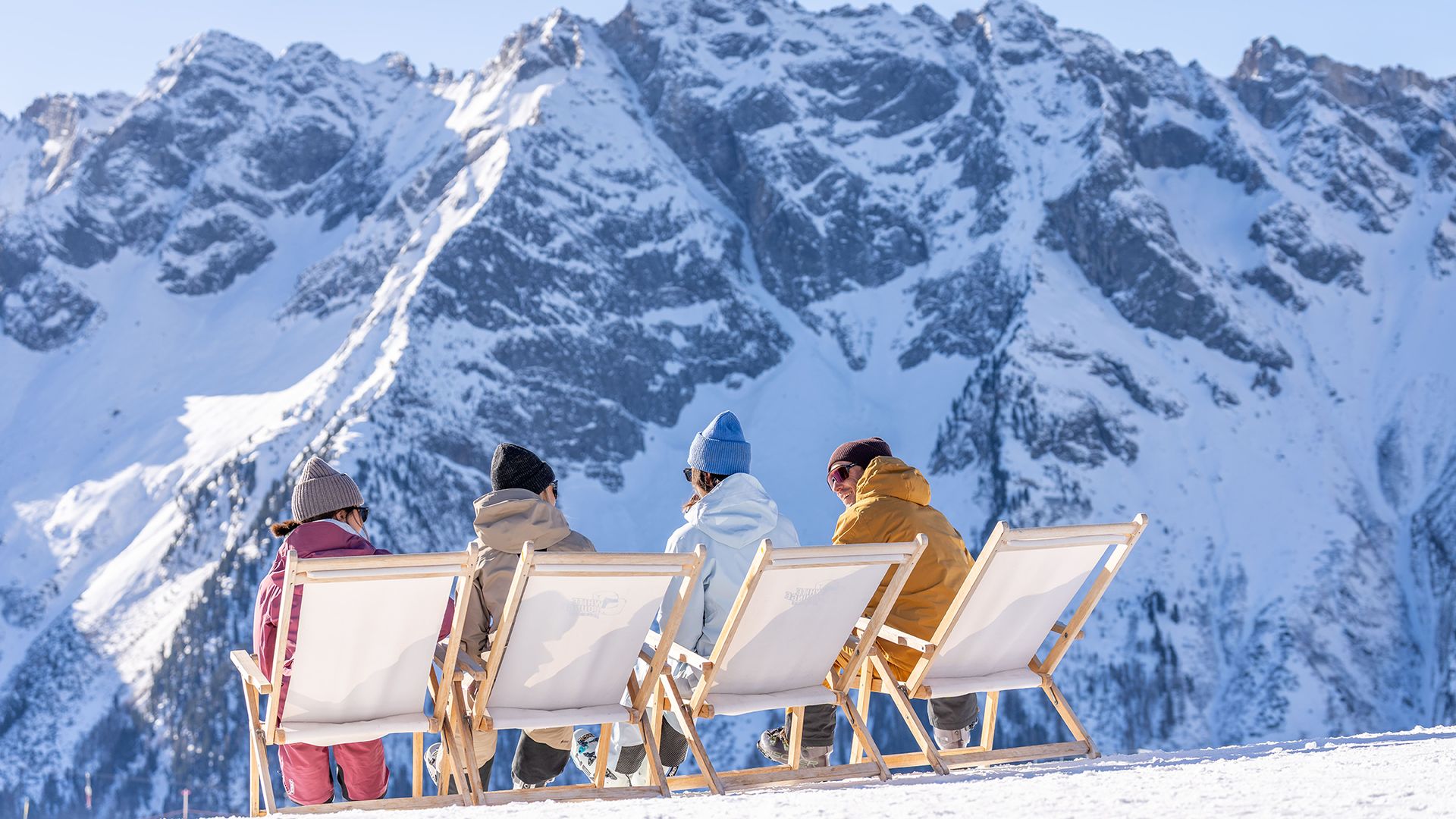 Freunde sitzen in Liegestühlen an der WhiteLounge SchneeBar am Ahorn