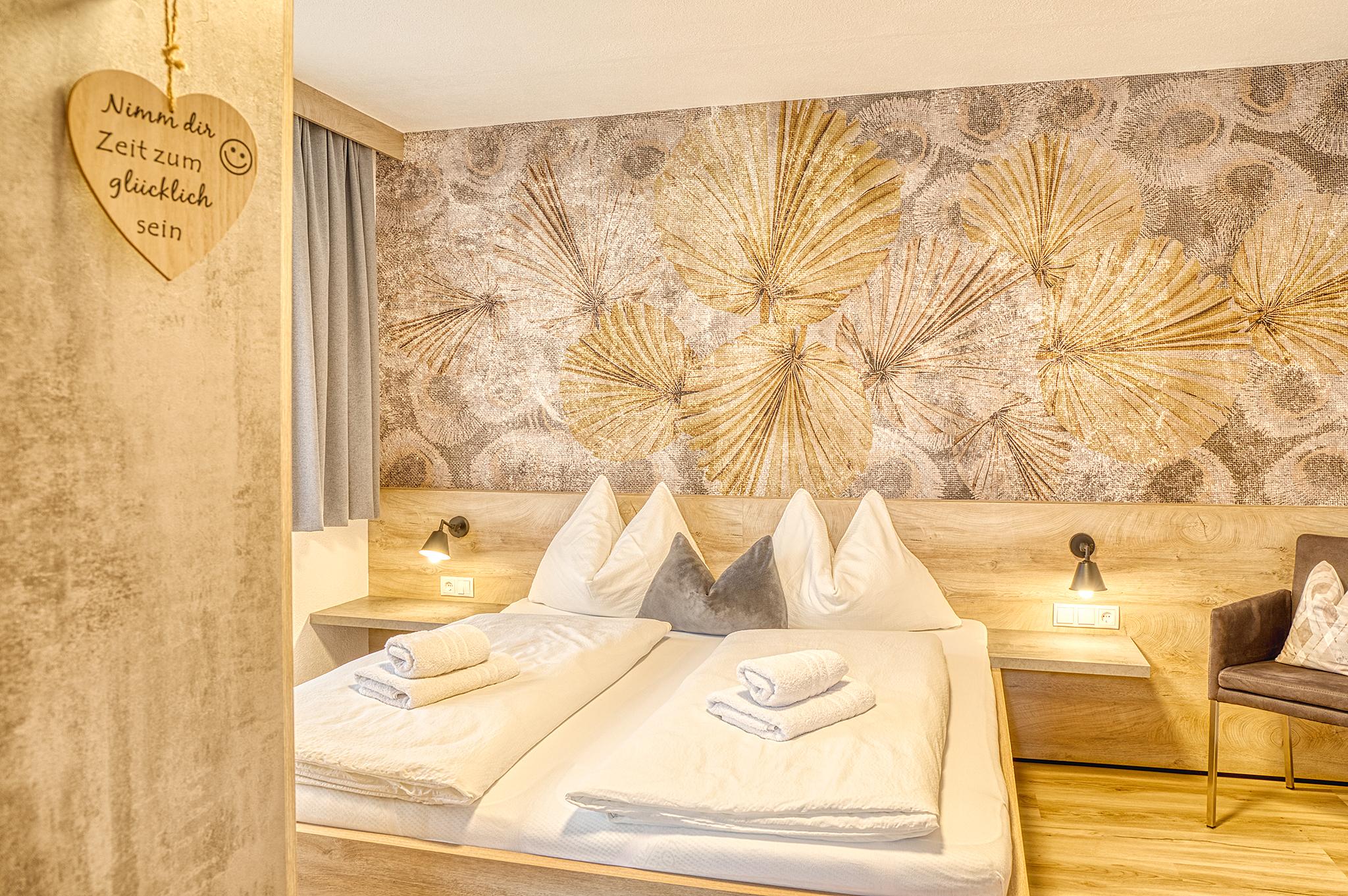 Hotel bed with white pillows, towels, and a wall mural of seashells in warm tones.