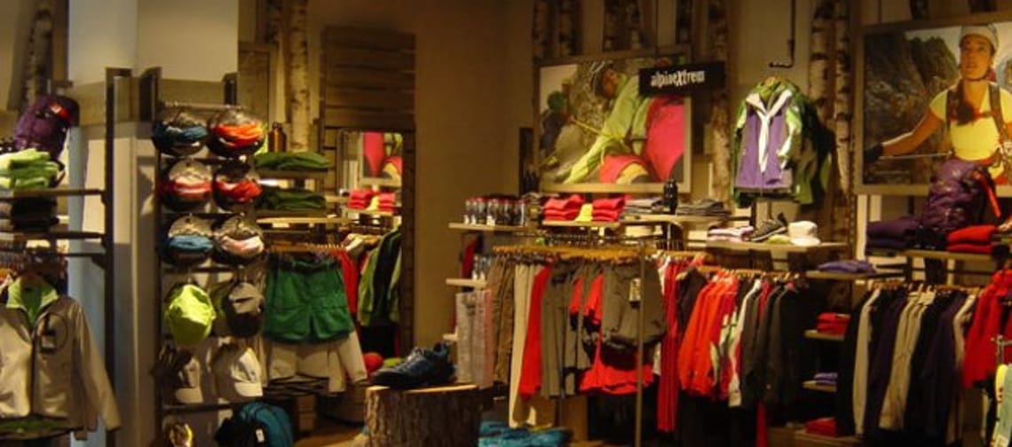 Sportbekleidung und Rucksäcke in einem Laden, mit Fotos an der Wand im Hintergrund.