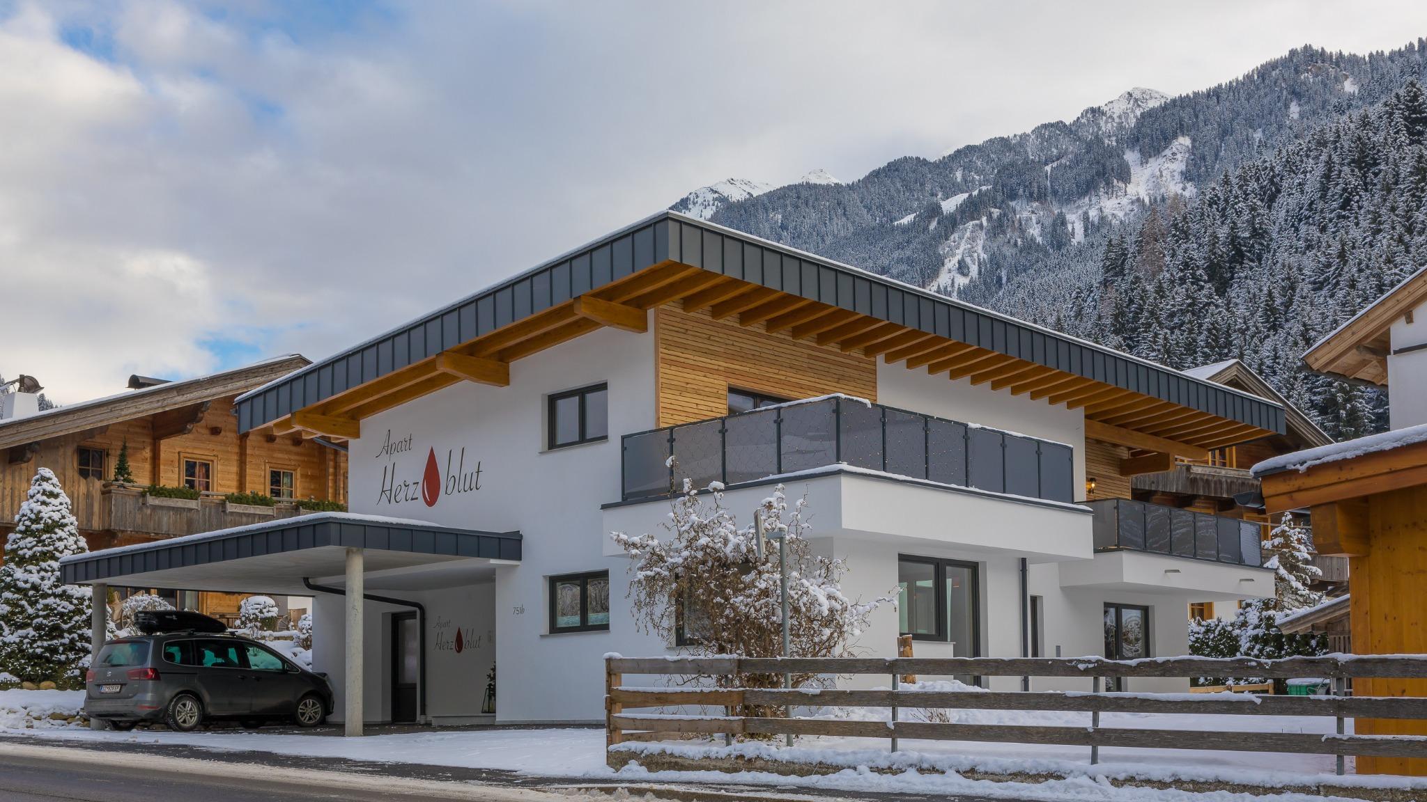 Modern white and wooden apartment with balcony in front of snowy mountain backdrop.