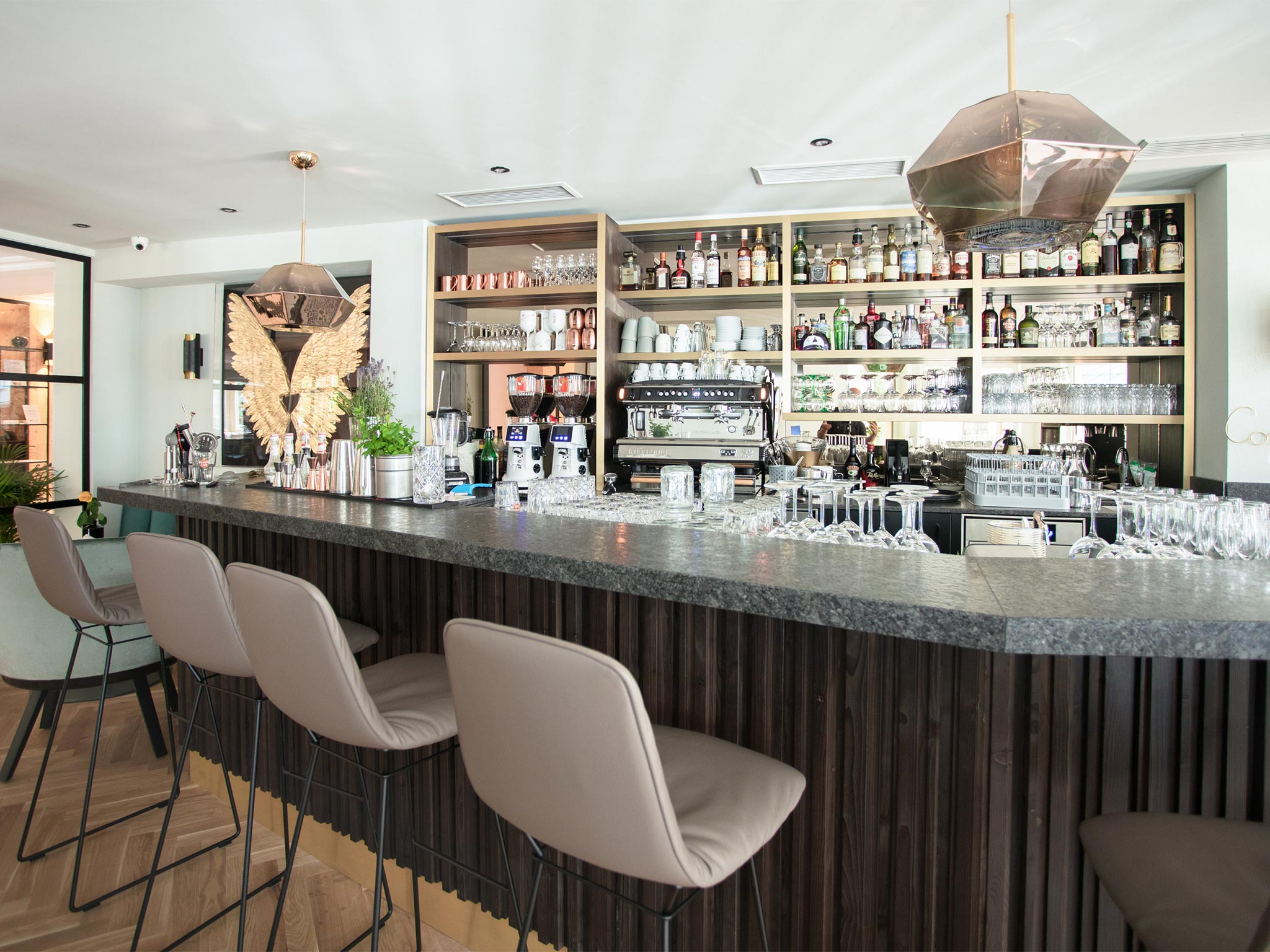 The image shows the Hof Bar – Wine & Cocktail Bar with its stylishly designed bar. The modern interior in shades of grey and black creates an elegant and tasteful ambiance