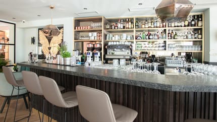 Das Bild zeigt die Hof Bar – Wine & Cocktailbar mit ihrer stilvoll gestalteten Bar. Das moderne Design in Grau- und Schwarztönen verleiht dem Raum eine edle und geschmackvolle Atmosphäre