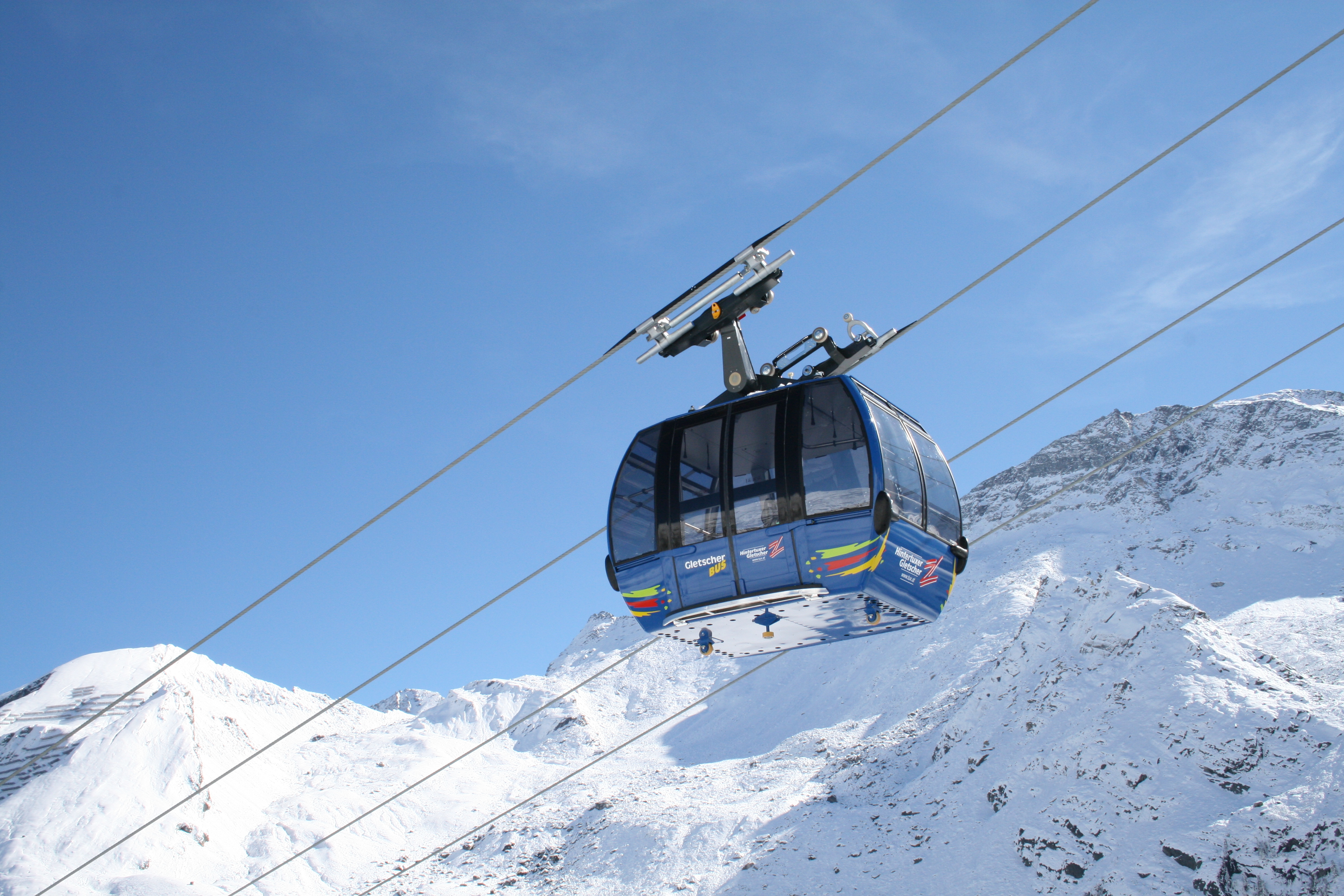 Gondelbahn fährt über schneebedeckte Berge bei klarem Himmel in den Alpen.
