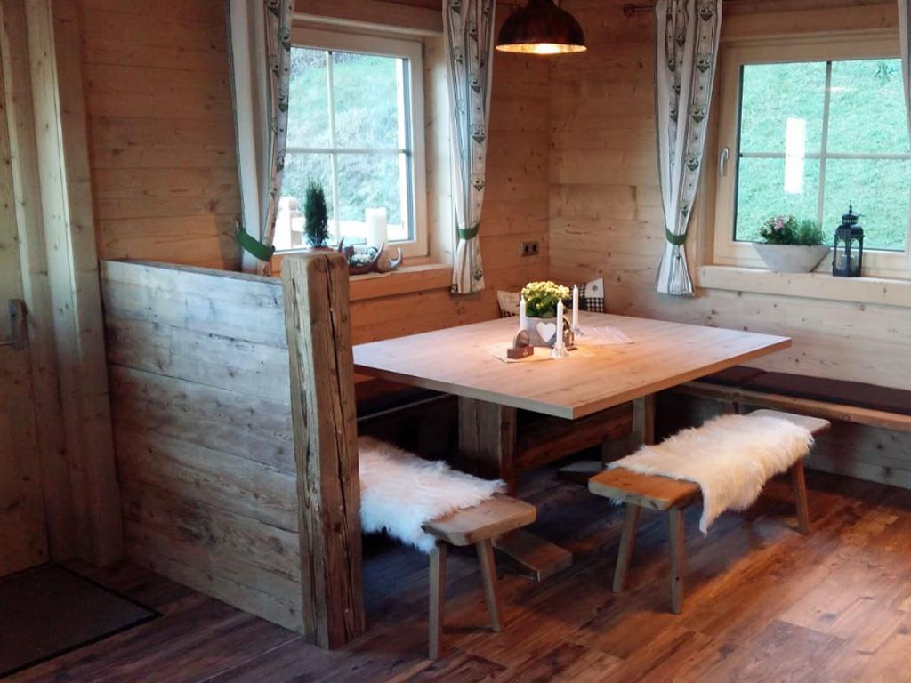 Cozy wooden dining nook with table, benches with sheepskin covers, and windows with curtains in a cabin.