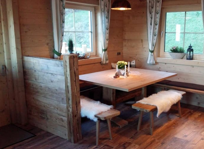 Gemütlicher Holz-Essbereich mit Tisch, Bänken, Sheepskin-Überzügen und Fenstern mit Vorhängen in einer Holzhütte.