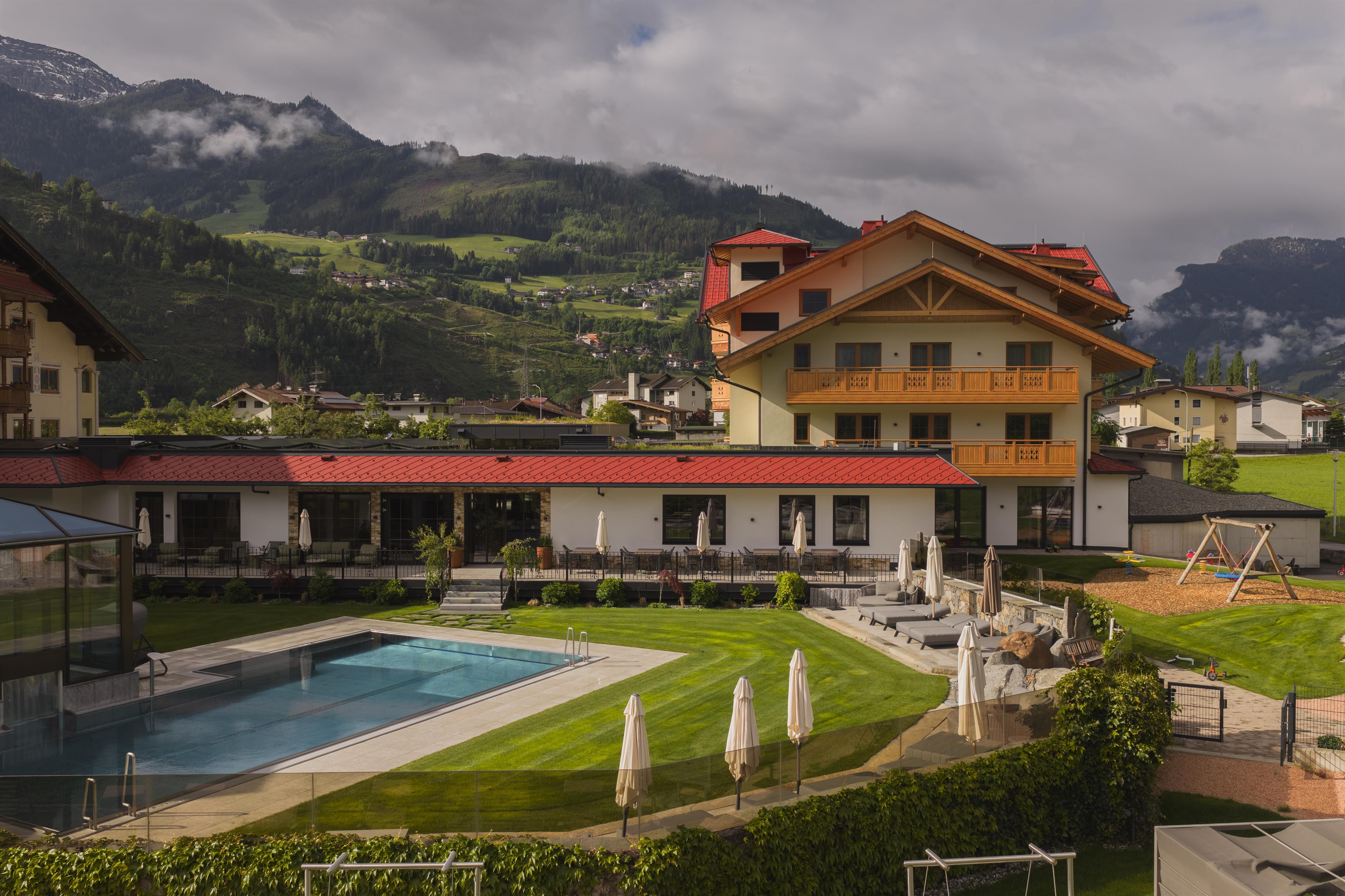 Ein moderner Pool im Garten mit Liegestühlen, umgeben von grünen Rasenflächen und einer Villa im Hintergrund.