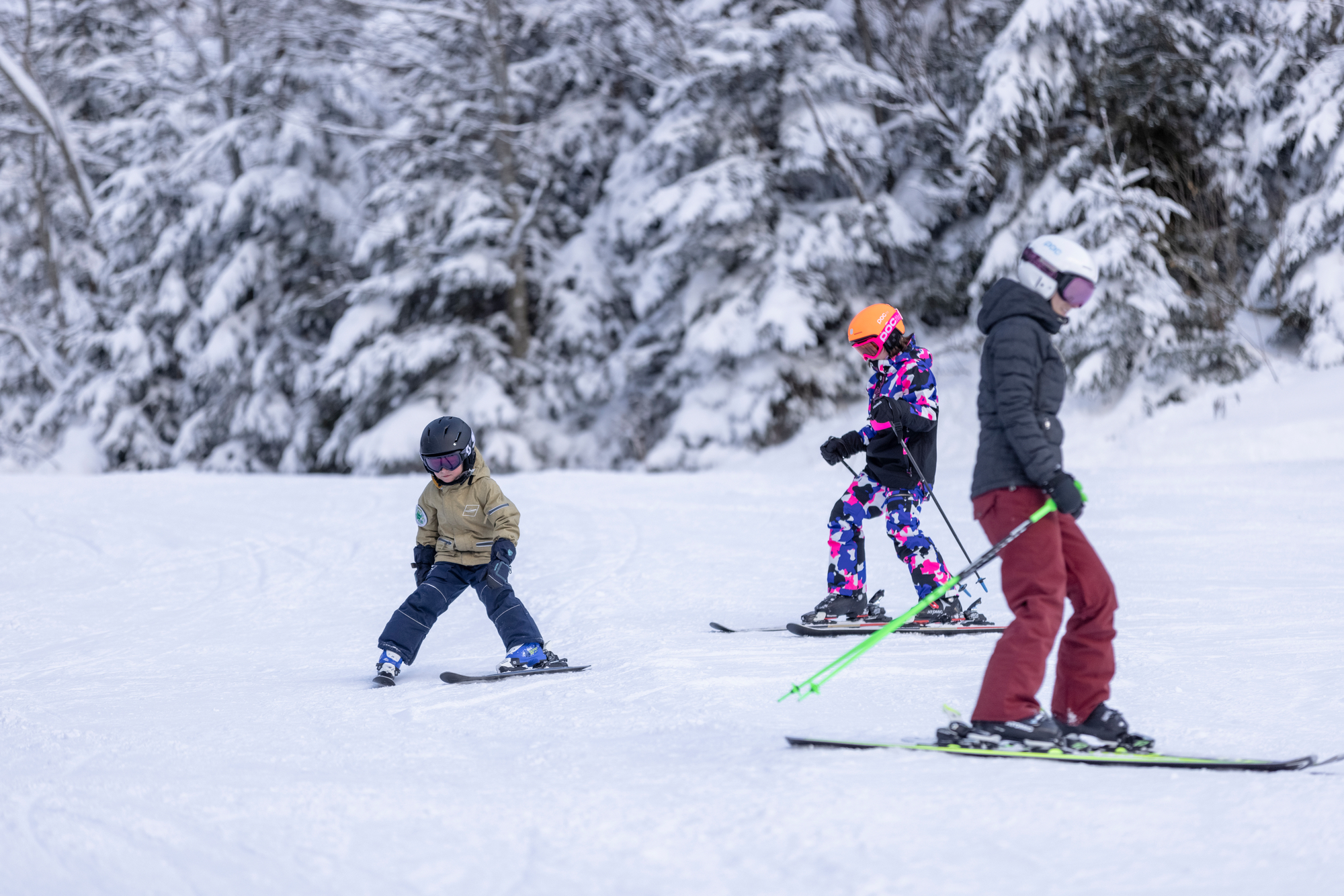 Adult with two children skiing at the Floitenlift in Ginzling in front of a snow-covered forest.