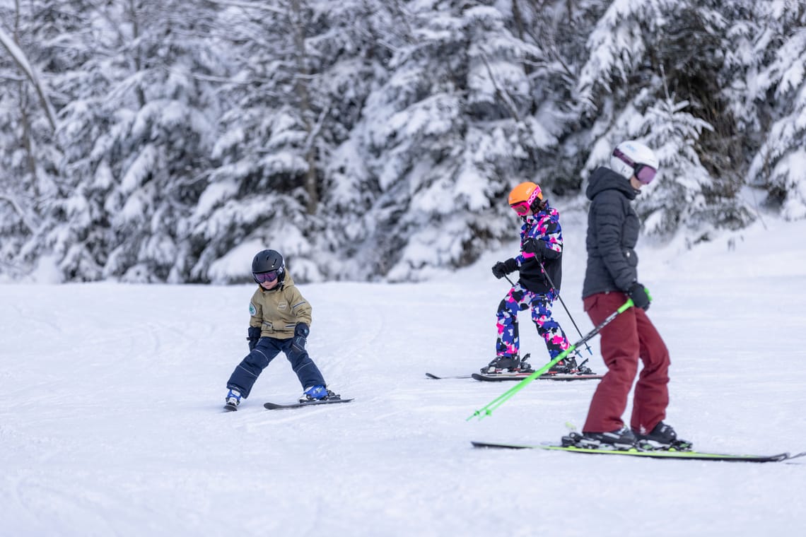 Skifahren in Ginzling Erwachsener mit zwei Kindern beim Skifahren am Floitenlift in Ginzling vor verschneitem Wald.