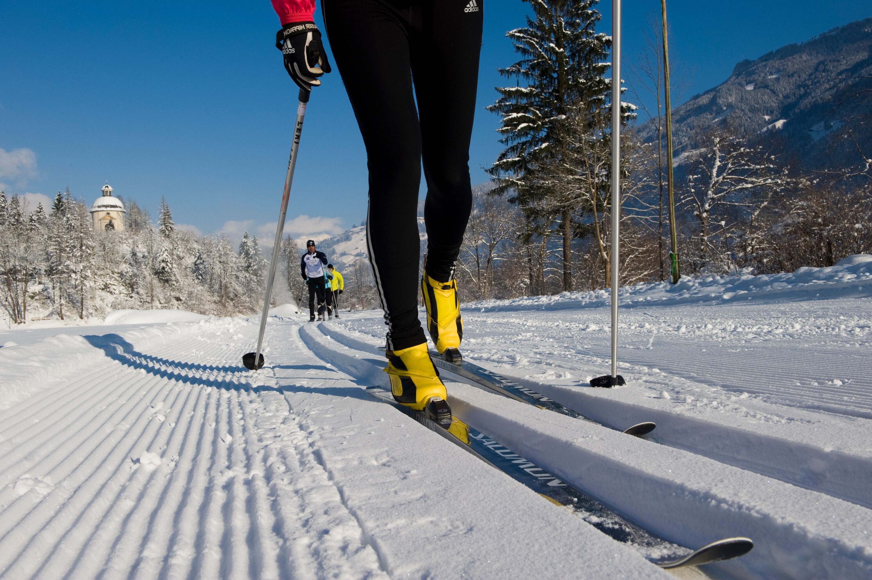 Close-up of a cross-country skier on a freshly groomed trail in Mayrhofen-Hippach, with yellow ski boots and snowy mountain scenery in the background.