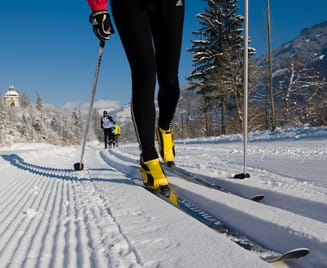 Close-up of a cross-country skier on a freshly groomed trail in Mayrhofen-Hippach, with yellow ski boots and snowy mountain scenery in the background.